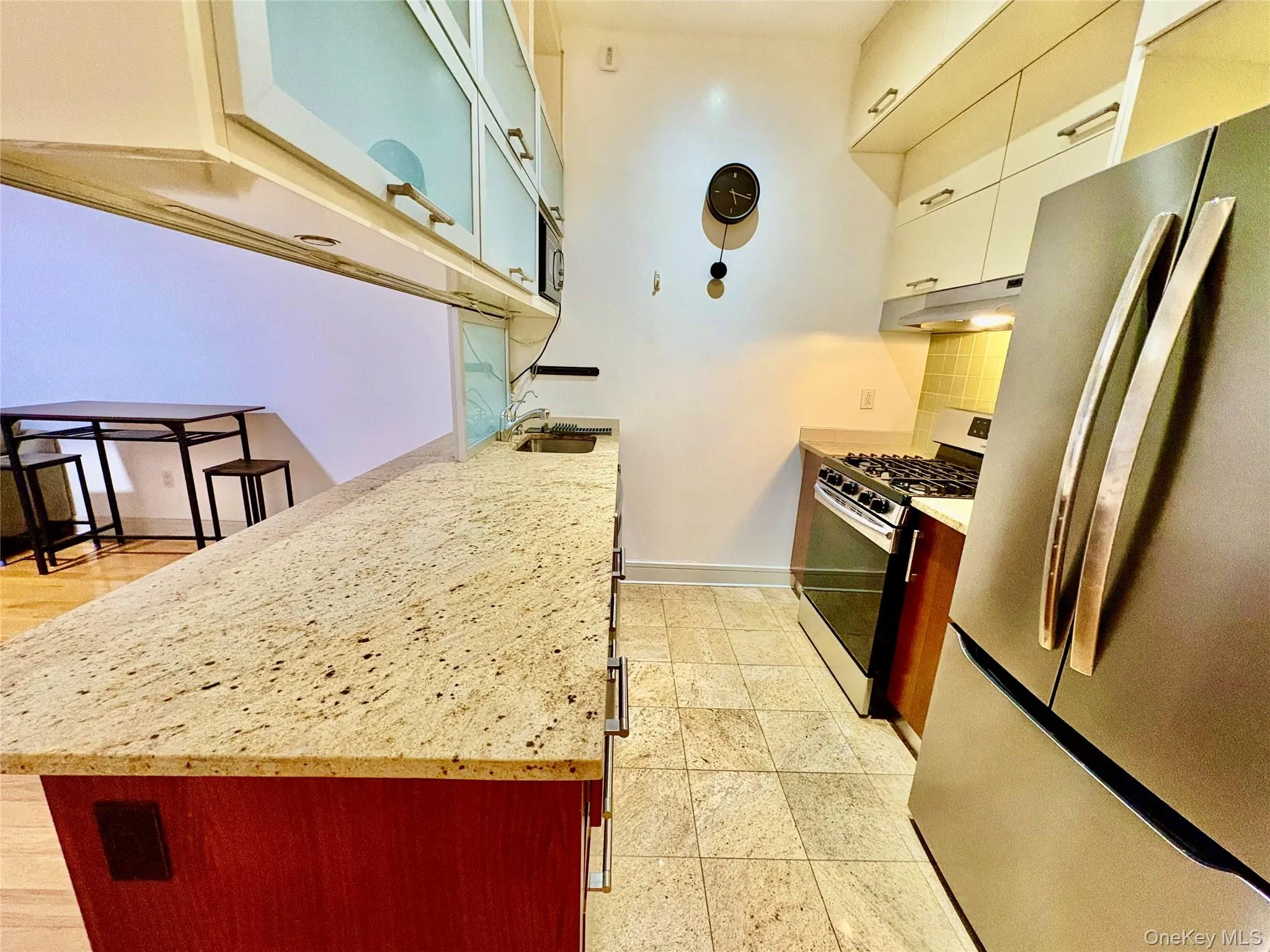 Kitchen with appliances with stainless steel finishes, light stone countertops, under cabinet range hood, glass insert cabinets, and tasteful backsplash Kitchen with appliances with stainless steel finishes, light stone countertops, under cabinet range hood, glass insert cabinets, and tasteful backsplash