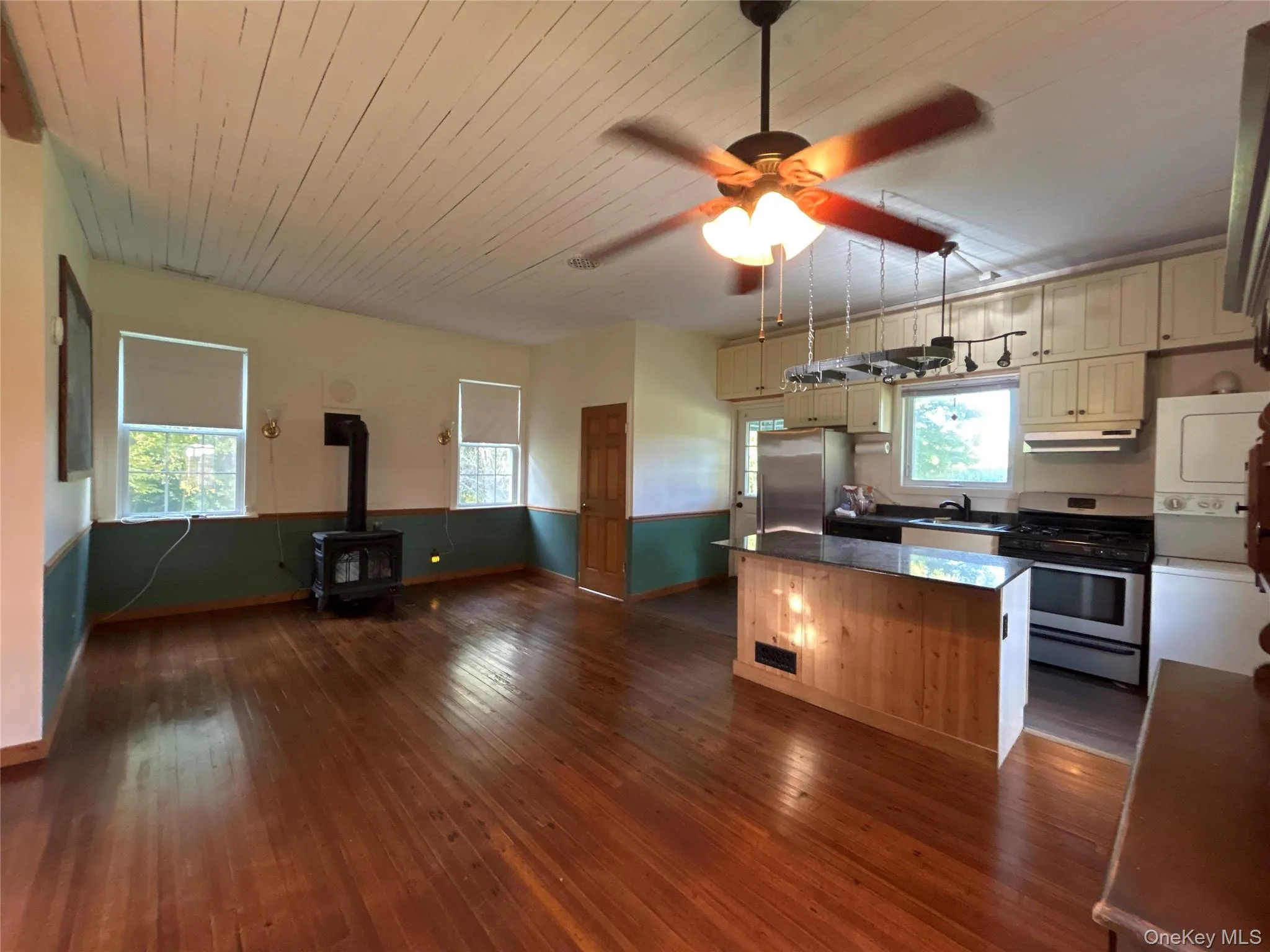 Kitchen featuring a wood stove, appliances with stainless steel finishes, washer / dryer, cream cabinets, and dark wood-style flooring Kitchen featuring a wood stove, appliances with stainless steel finishes, washer / dryer, cream cabinets, and dark wood-style flooring