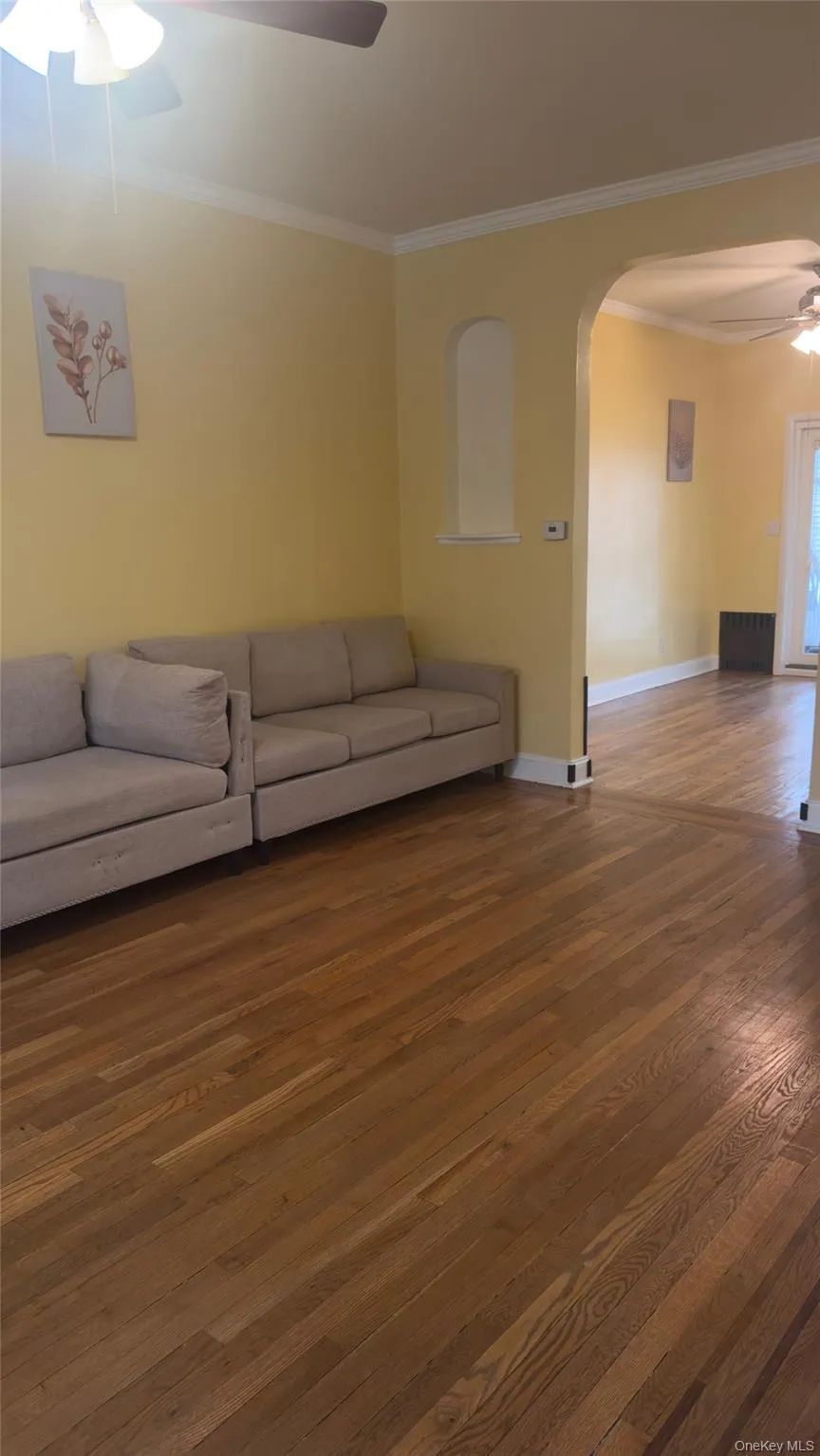 Living room featuring ceiling fan, crown molding, arched walkways, and wood-type flooring Living room featuring ceiling fan, crown molding, arched walkways, and wood-type flooring