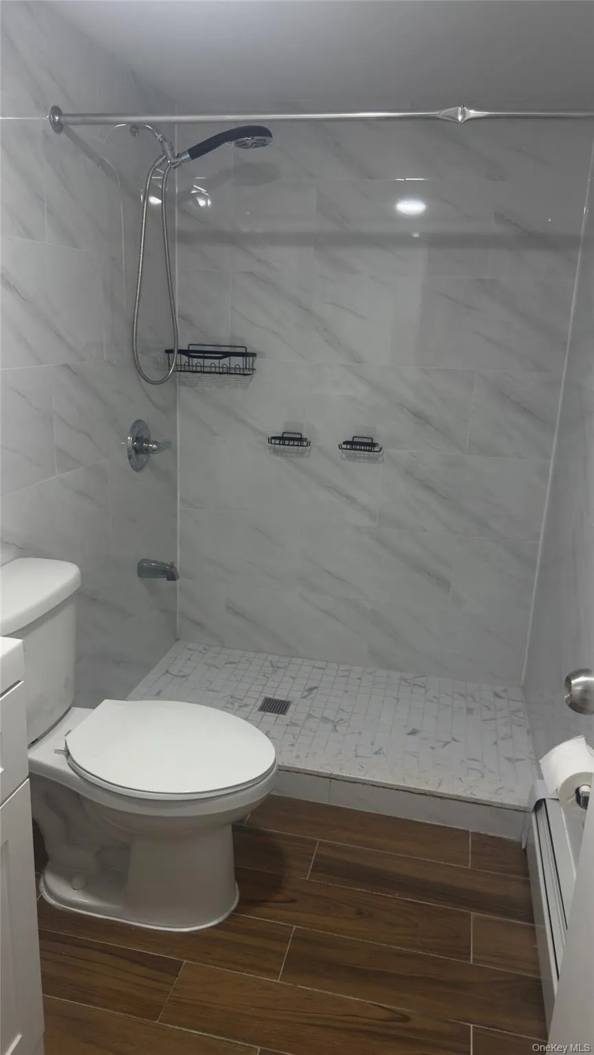 Full bathroom featuring wood finish floors, a stall shower, vanity, and a baseboard heating unit Full bathroom featuring wood finish floors, a stall shower, vanity, and a baseboard heating unit