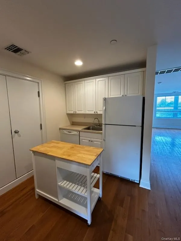 Kitchen featuring white appliances, white cabinetry, dark wood finished floors, wood counters, and recessed lighting Kitchen featuring white appliances, white cabinetry, dark wood finished floors, wood counters, and recessed lighting