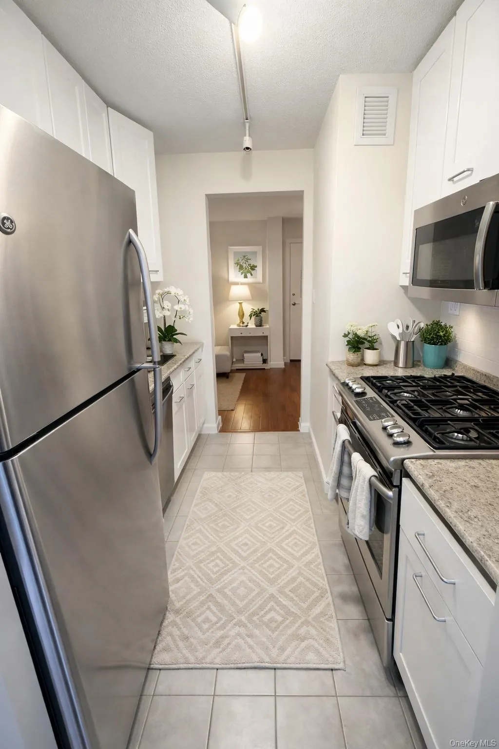 Kitchen with appliances with stainless steel finishes, white cabinets, light stone countertops, light tile patterned floors, and a textured ceiling Kitchen with appliances with stainless steel finishes, white cabinets, light stone countertops, light tile patterned floors, and a textured ceiling