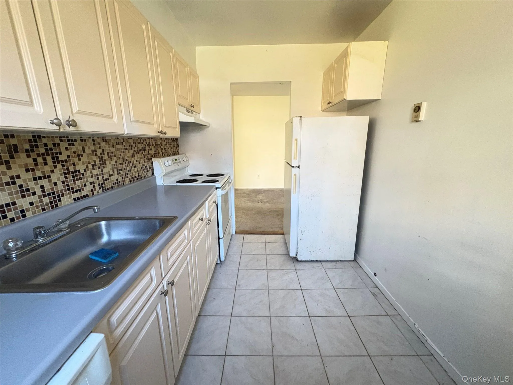 Kitchen featuring white appliances, light tile patterned flooring, tasteful backsplash, under cabinet range hood, and white cabinets Kitchen featuring white appliances, light tile patterned flooring, tasteful backsplash, under cabinet range hood, and white cabinets