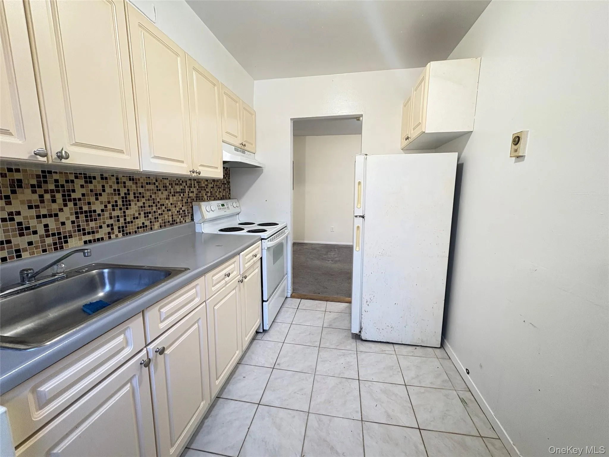 Kitchen with white appliances, light tile patterned floors, tasteful backsplash, and under cabinet range hood Kitchen with white appliances, light tile patterned floors, tasteful backsplash, and under cabinet range hood