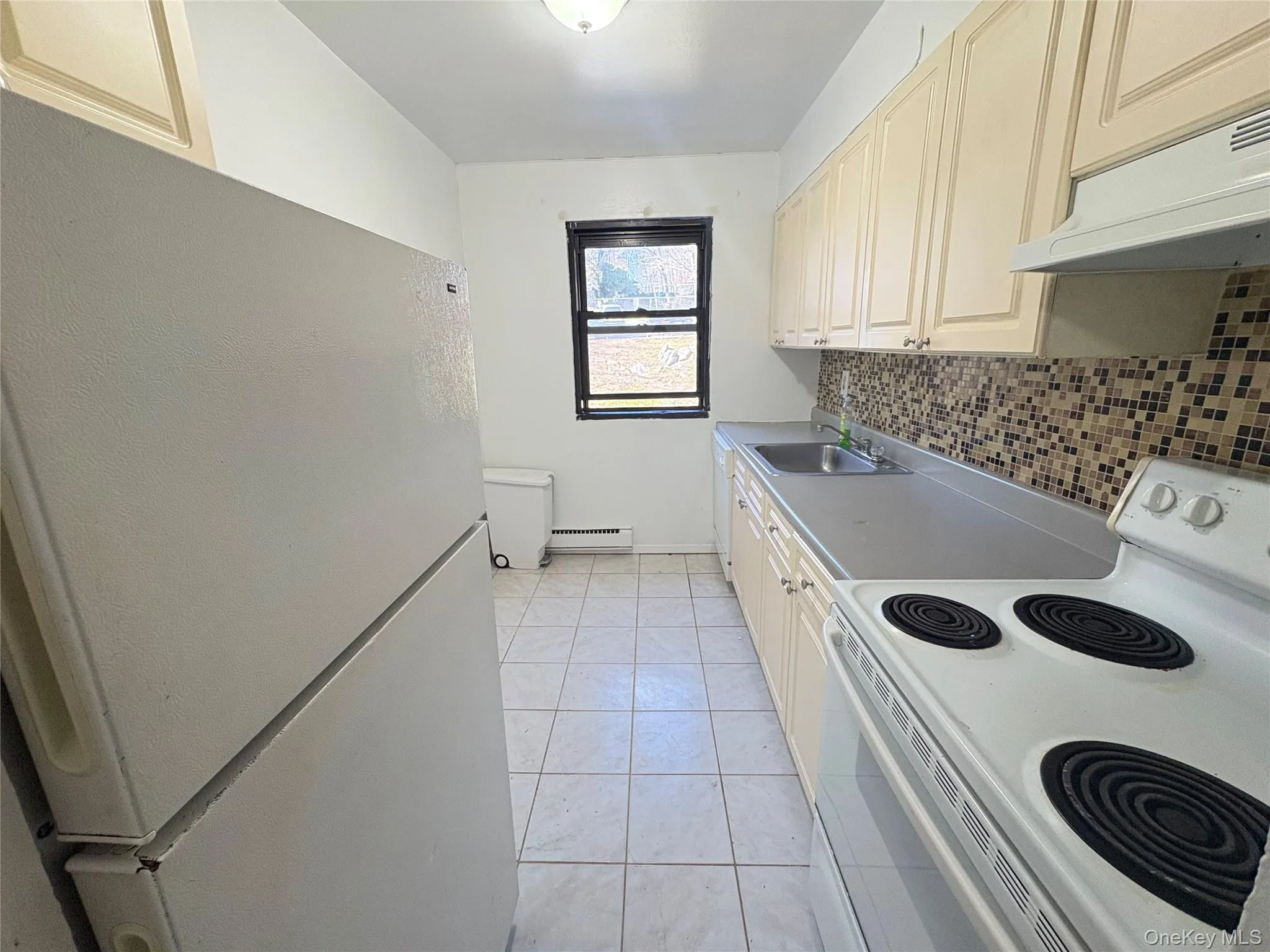 Kitchen with white appliances, under cabinet range hood, light countertops, light tile patterned flooring, and a baseboard radiator Kitchen with white appliances, under cabinet range hood, light countertops, light tile patterned flooring, and a baseboard radiator