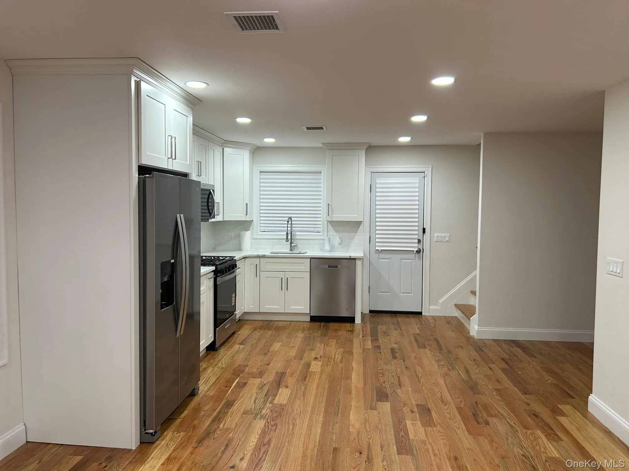 Kitchen with white cabinets, stainless steel appliances, dark wood-style flooring, backsplash, and recessed lighting Kitchen with white cabinets, stainless steel appliances, dark wood-style flooring, backsplash, and recessed lighting