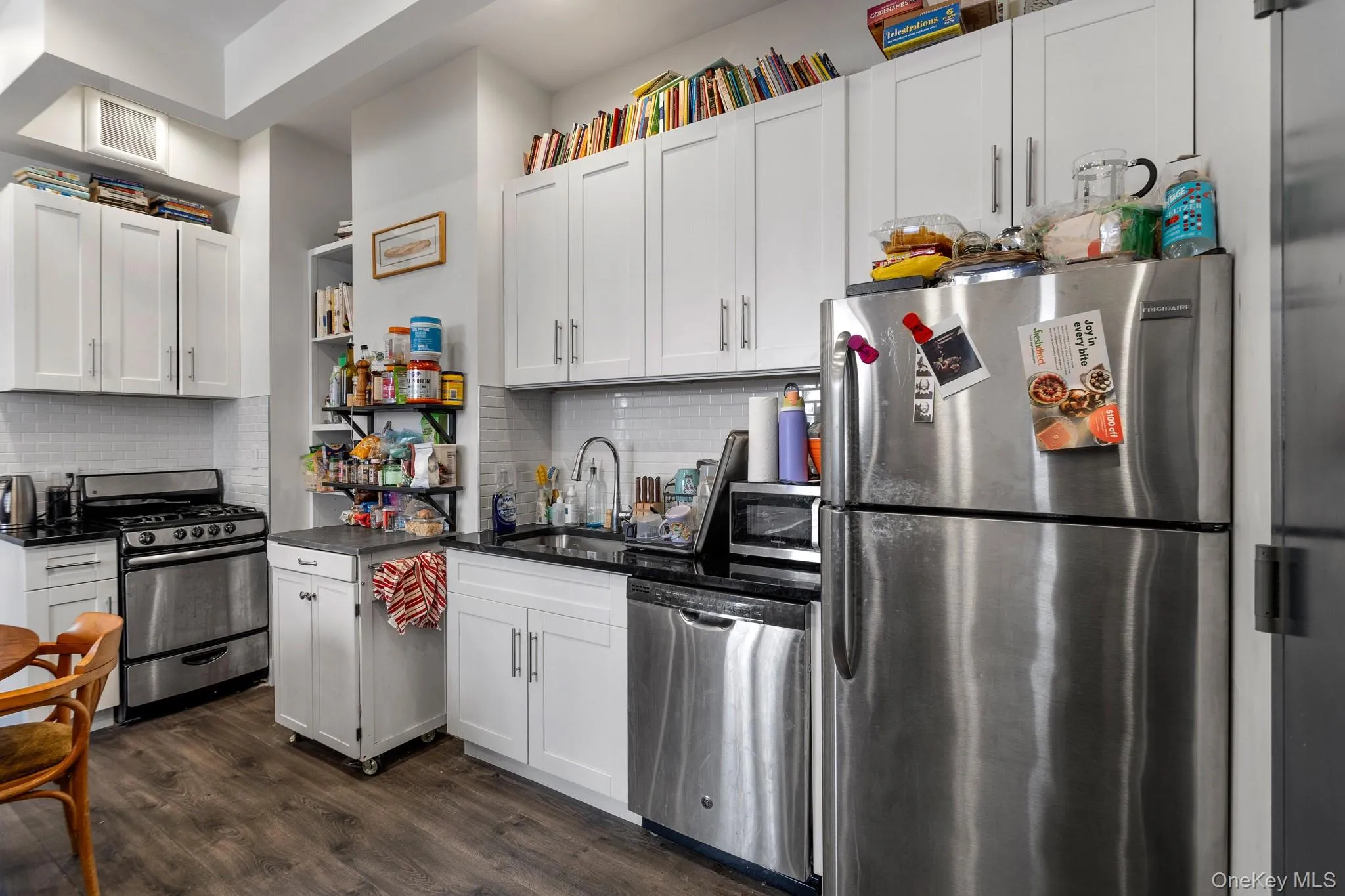 Kitchen featuring appliances with stainless steel finishes, white cabinetry, dark wood-style floors, and dark stone counters Kitchen featuring appliances with stainless steel finishes, white cabinetry, dark wood-style floors, and dark stone counters
