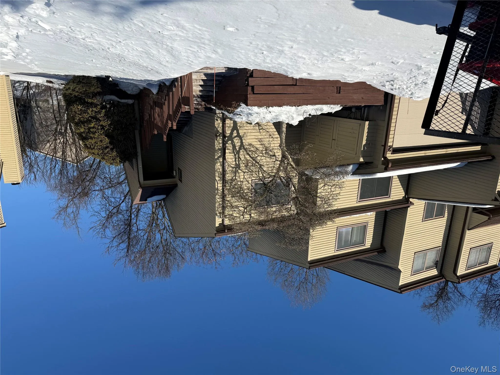 Modern multi-level townhome featuring tan vinyl siding, a private garage, and an elevated entryway with a wooden staircase. Modern multi-level townhome featuring tan vinyl siding, a private garage, and an elevated entryway with a wooden staircase.