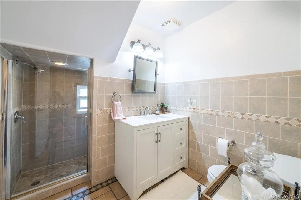 Bathroom featuring light tile patterned flooring, vanity, tile walls, a stall shower, and a wainscoted wall Bathroom featuring light tile patterned flooring, vanity, tile walls, a stall shower, and a wainscoted wall