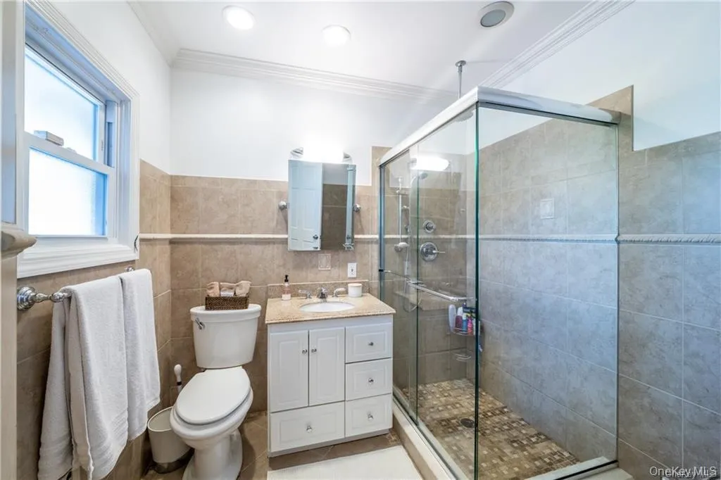 Bathroom featuring vanity, ornamental molding, a shower stall, tile walls, and wainscoting Bathroom featuring vanity, ornamental molding, a shower stall, tile walls, and wainscoting