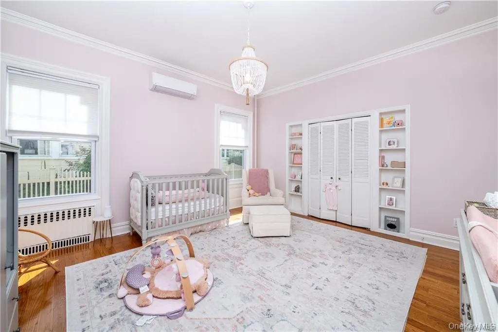 Bedroom featuring radiator heating unit, a nursery area, a wall mounted AC, crown molding, and a chandelier Bedroom featuring radiator heating unit, a nursery area, a wall mounted AC, crown molding, and a chandelier