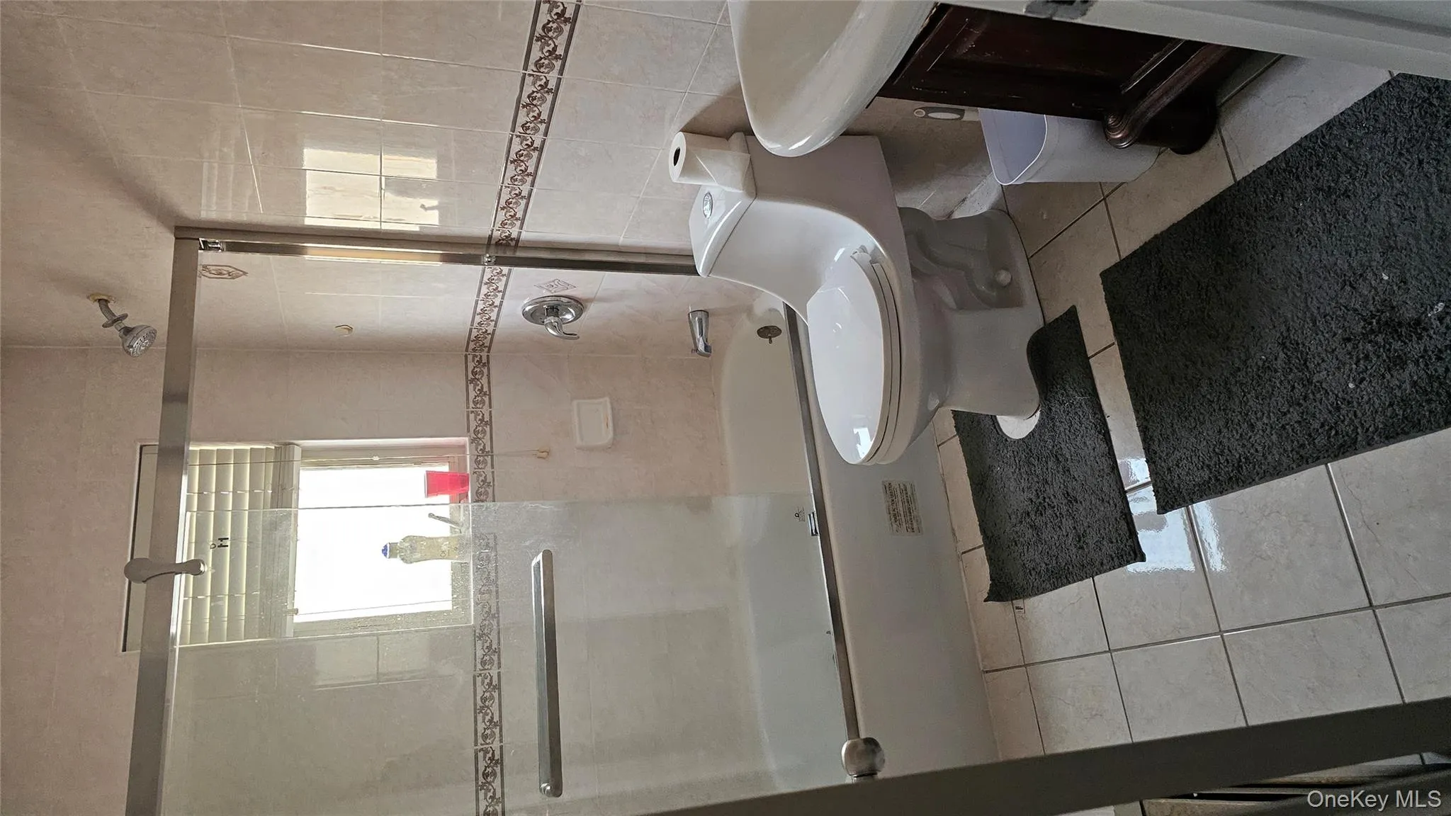 Full bathroom with tile walls, bath / shower combo with glass door, vanity, and light tile patterned floors Full bathroom with tile walls, bath / shower combo with glass door, vanity, and light tile patterned floors