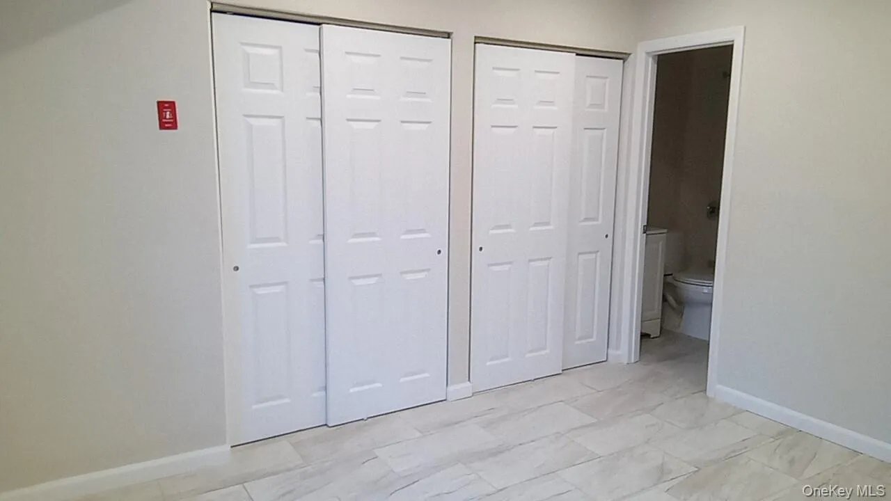 Unfurnished bedroom with multiple closets, ensuite bathroom, and light marble finish floors Unfurnished bedroom with multiple closets, ensuite bathroom, and light marble finish floors