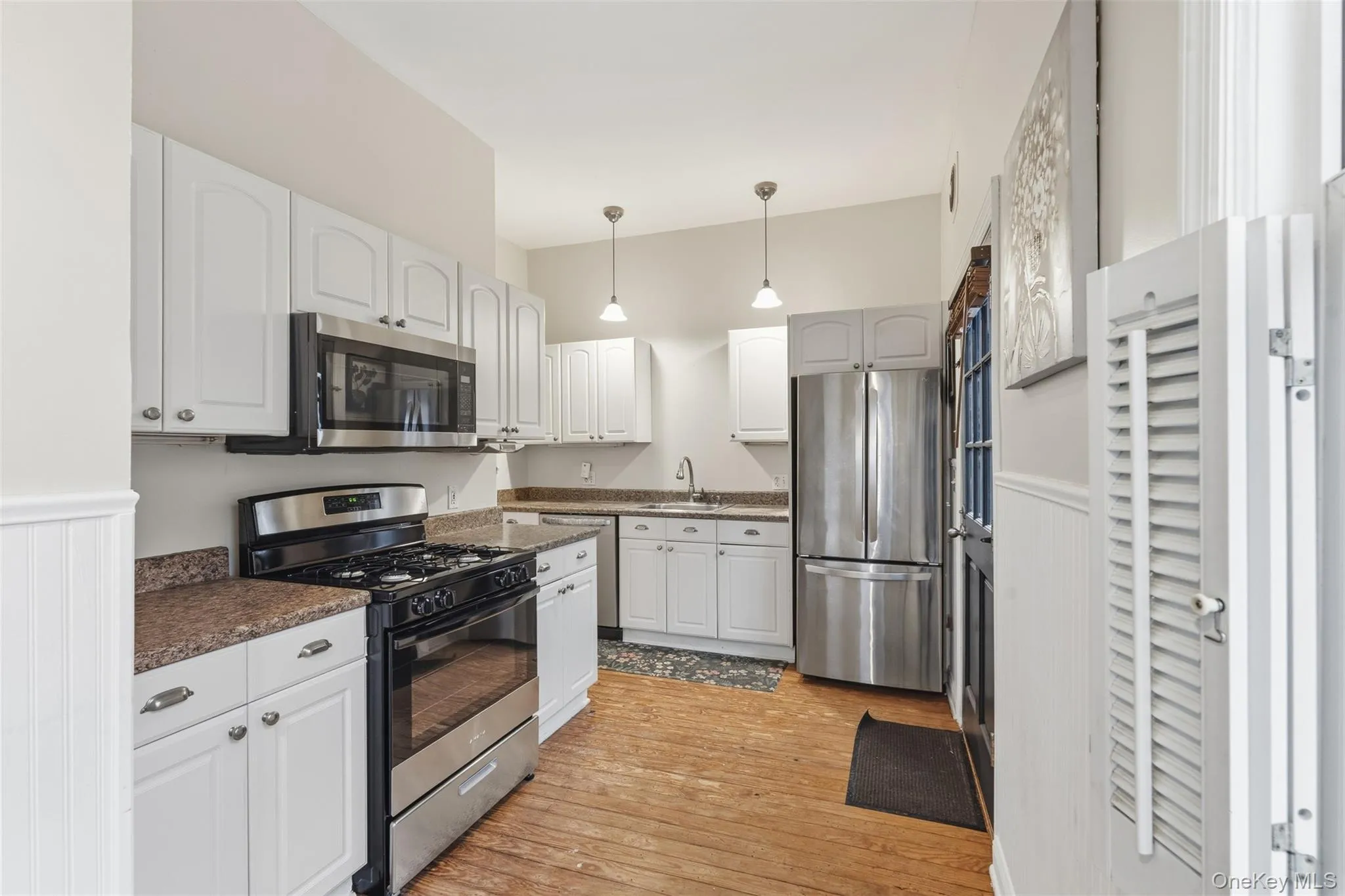 Kitchen featuring appliances with stainless steel finishes, white cabinetry, hanging light fixtures, light wood-style floors, and dark stone countertops Kitchen featuring appliances with stainless steel finishes, white cabinetry, hanging light fixtures, light wood-style floors, and dark stone countertops