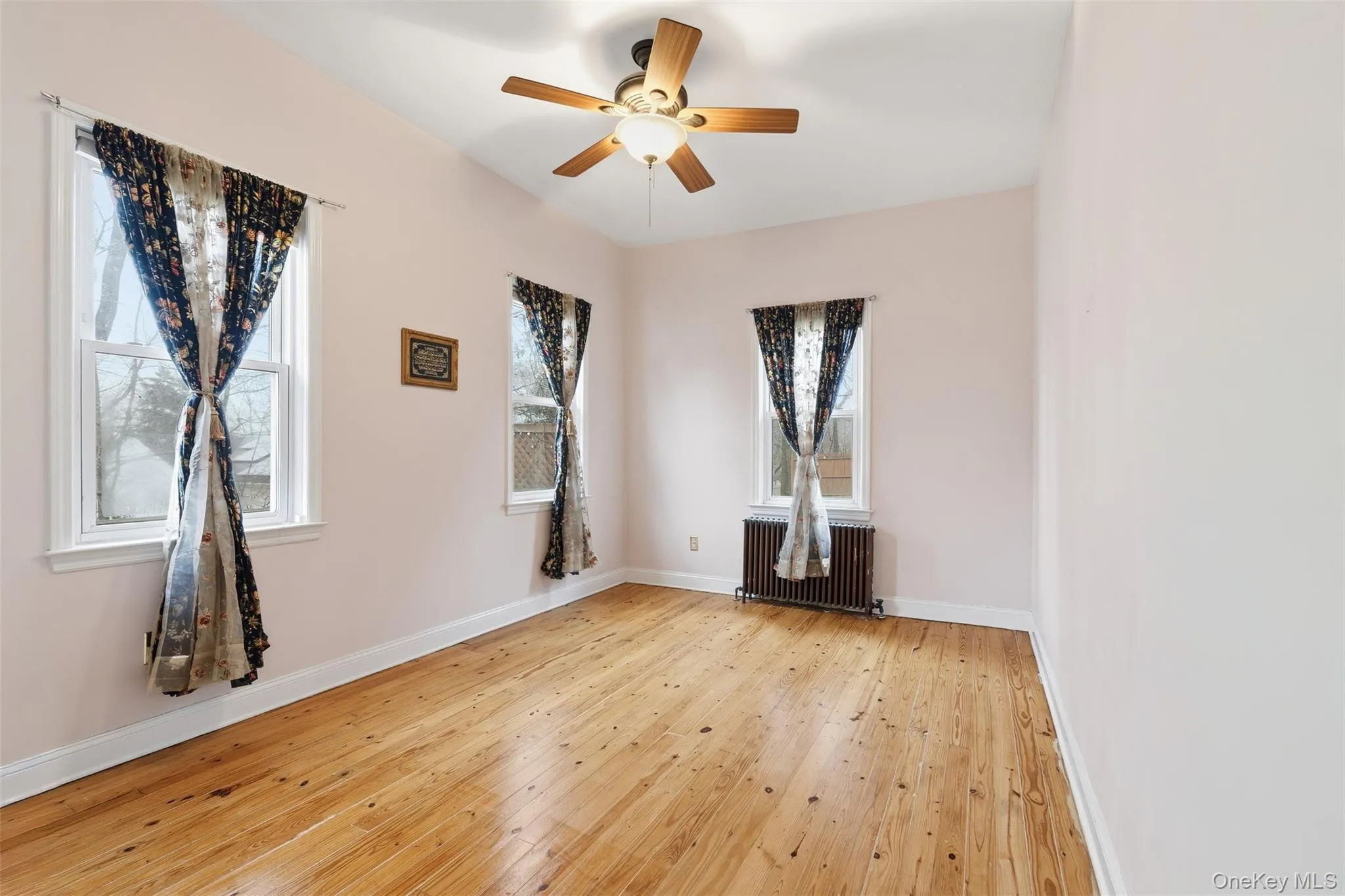Unfurnished room with light wood-style flooring, radiator, and ceiling fan Unfurnished room with light wood-style flooring, radiator, and ceiling fan