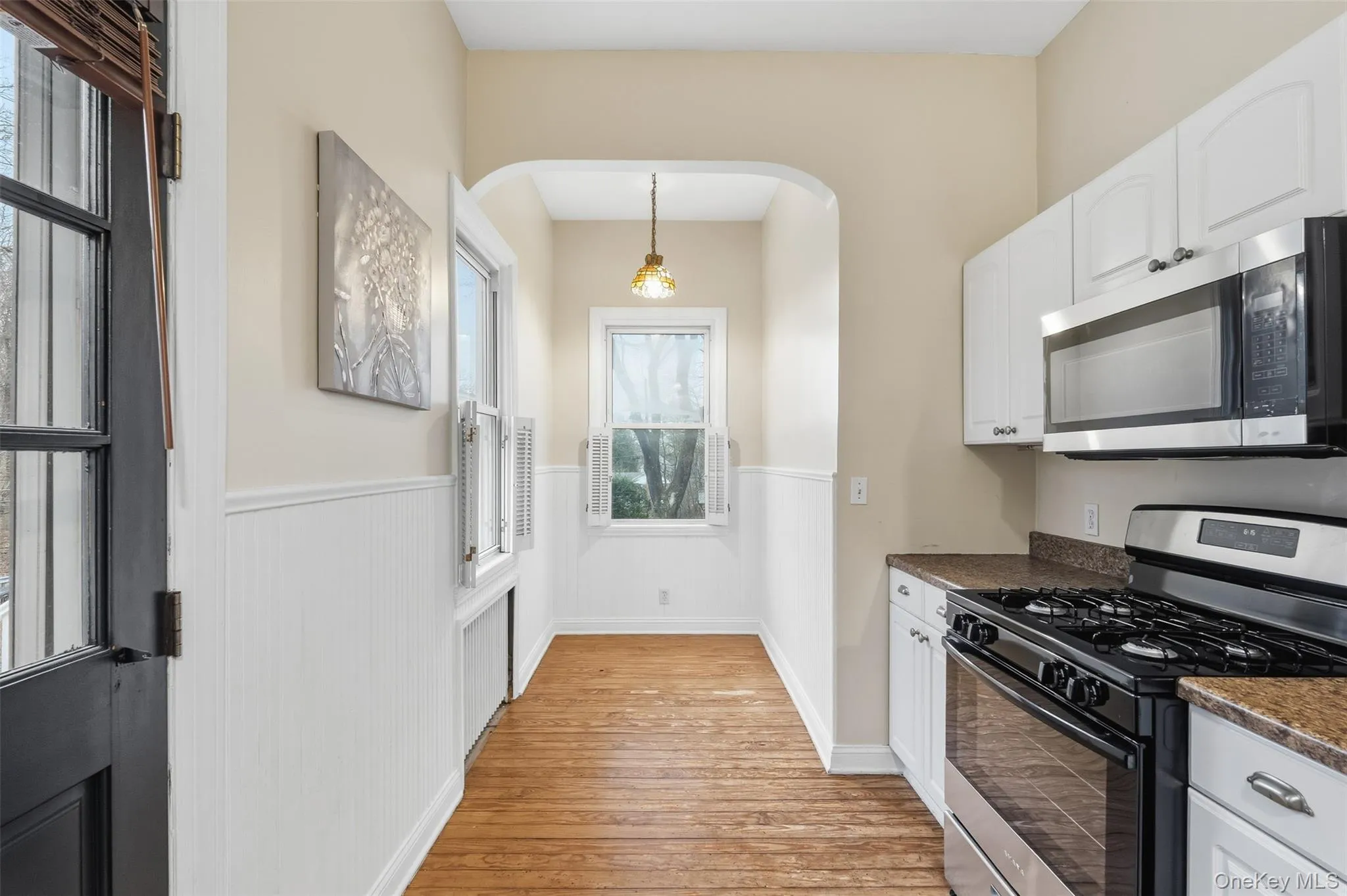 Kitchen with range with gas cooktop, a wainscoted wall, white cabinets, stainless steel microwave, and hanging light fixtures Kitchen with range with gas cooktop, a wainscoted wall, white cabinets, stainless steel microwave, and hanging light fixtures