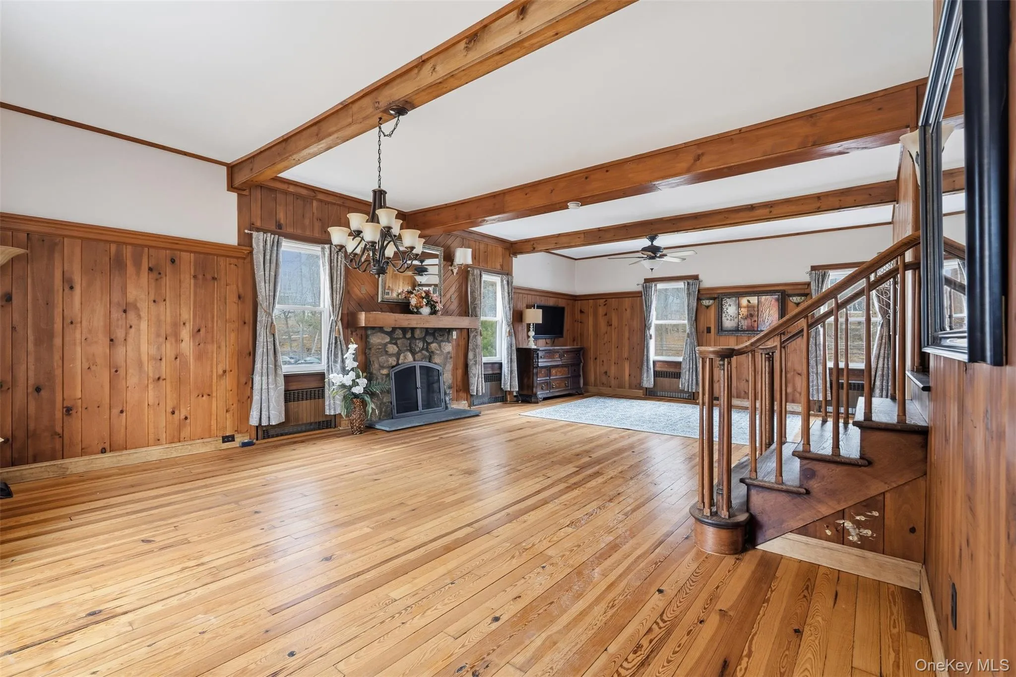 Unfurnished living room featuring a fireplace, a chandelier, wood walls, light wood-style flooring, and stairway Unfurnished living room featuring a fireplace, a chandelier, wood walls, light wood-style flooring, and stairway