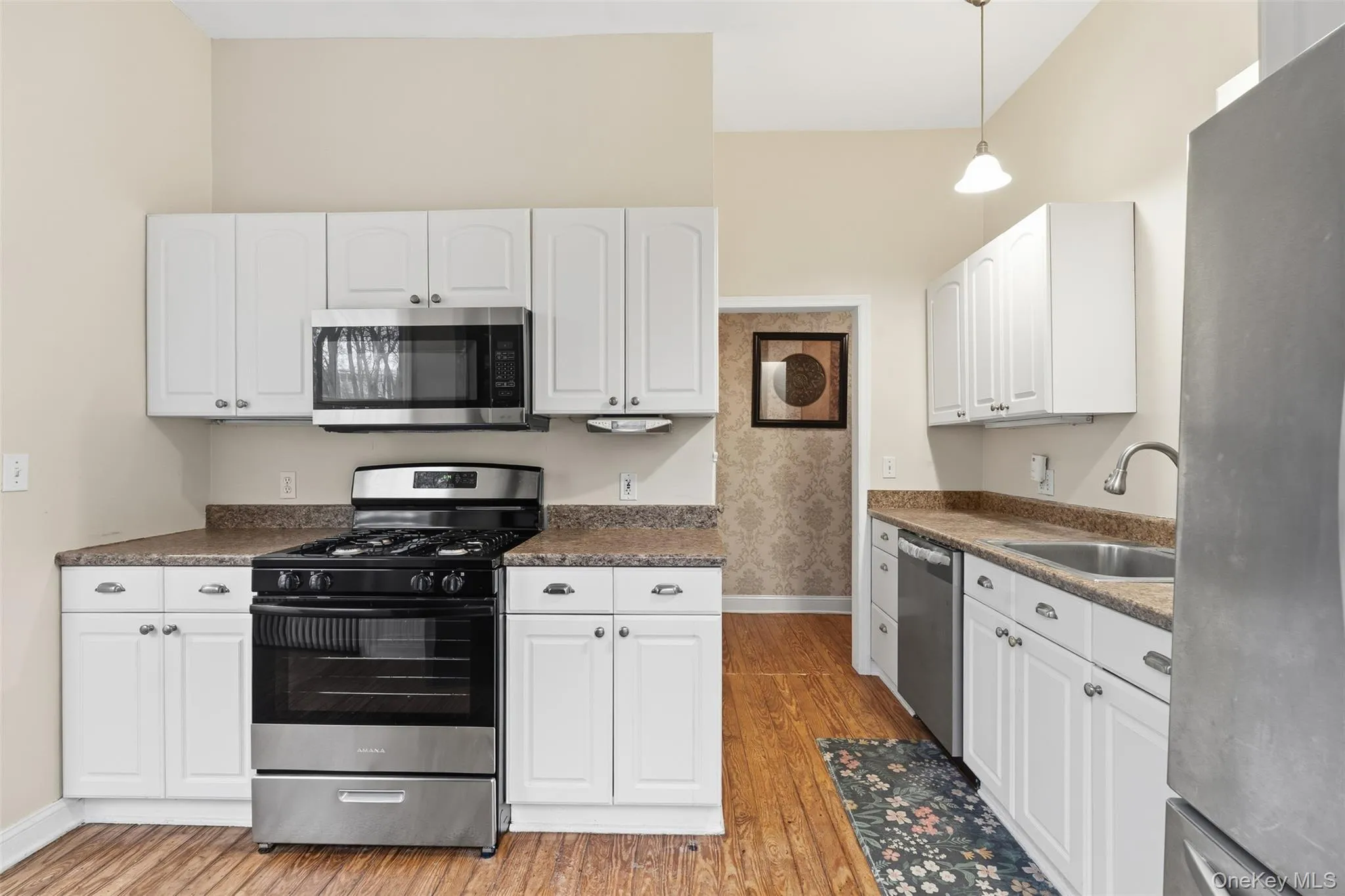 Kitchen featuring stainless steel appliances, white cabinets, dark countertops, and decorative light fixtures Kitchen featuring stainless steel appliances, white cabinets, dark countertops, and decorative light fixtures