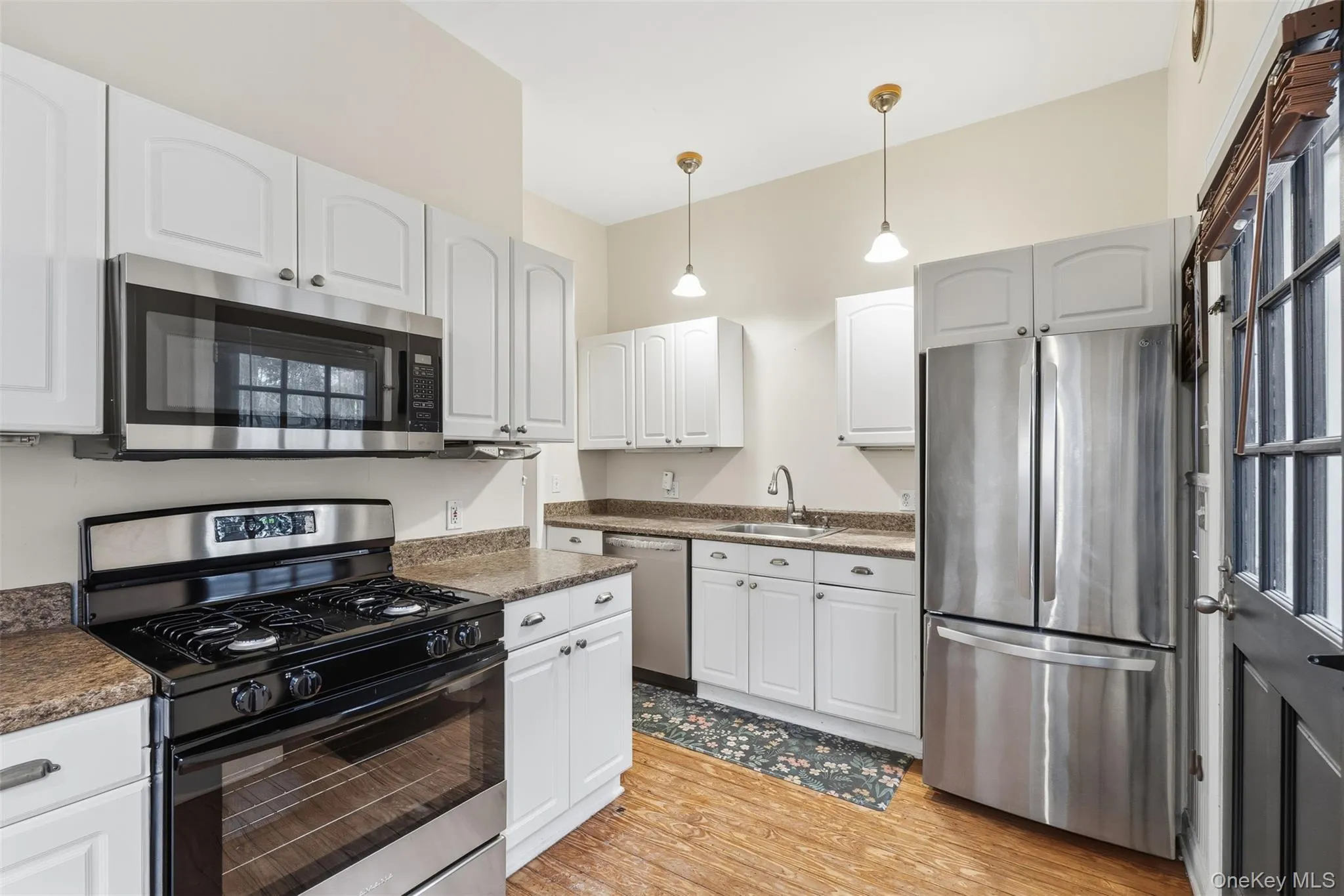 Kitchen with appliances with stainless steel finishes, white cabinetry, pendant lighting, and light wood-type flooring Kitchen with appliances with stainless steel finishes, white cabinetry, pendant lighting, and light wood-type flooring