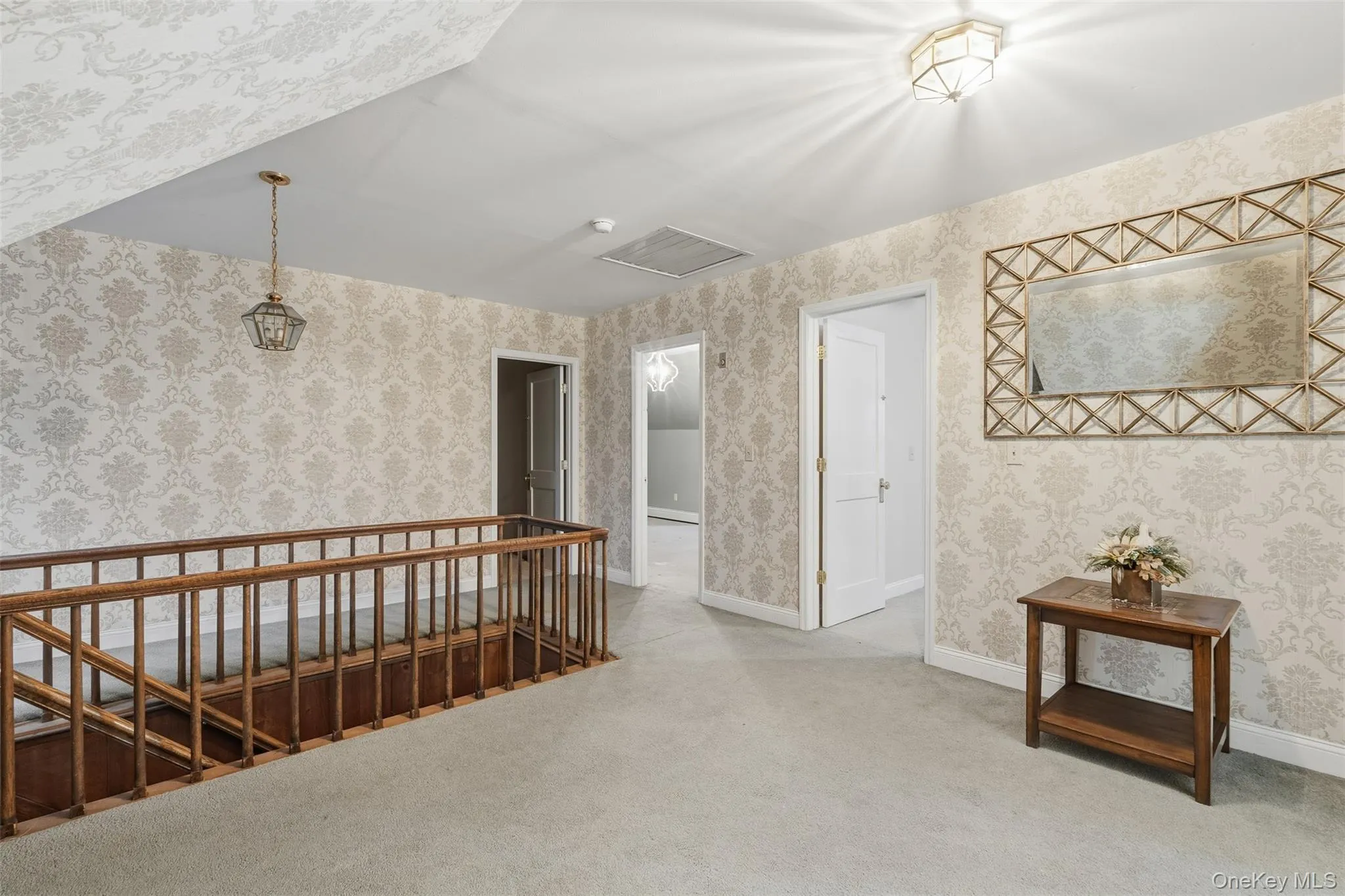 Hall with an upstairs landing, wallpapered walls, and light colored carpet Hall with an upstairs landing, wallpapered walls, and light colored carpet