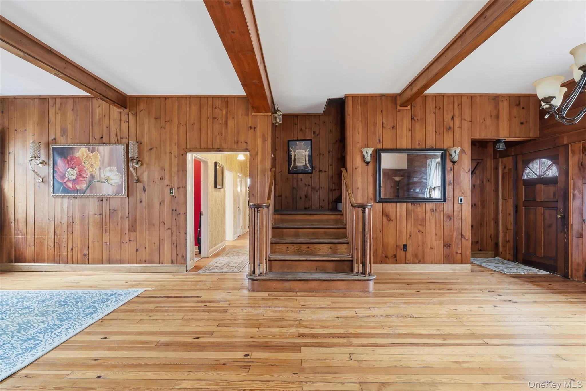 Entrance foyer with wooden walls, light wood-type flooring, stairway, beamed ceiling, and a chandelier Entrance foyer with wooden walls, light wood-type flooring, stairway, beamed ceiling, and a chandelier