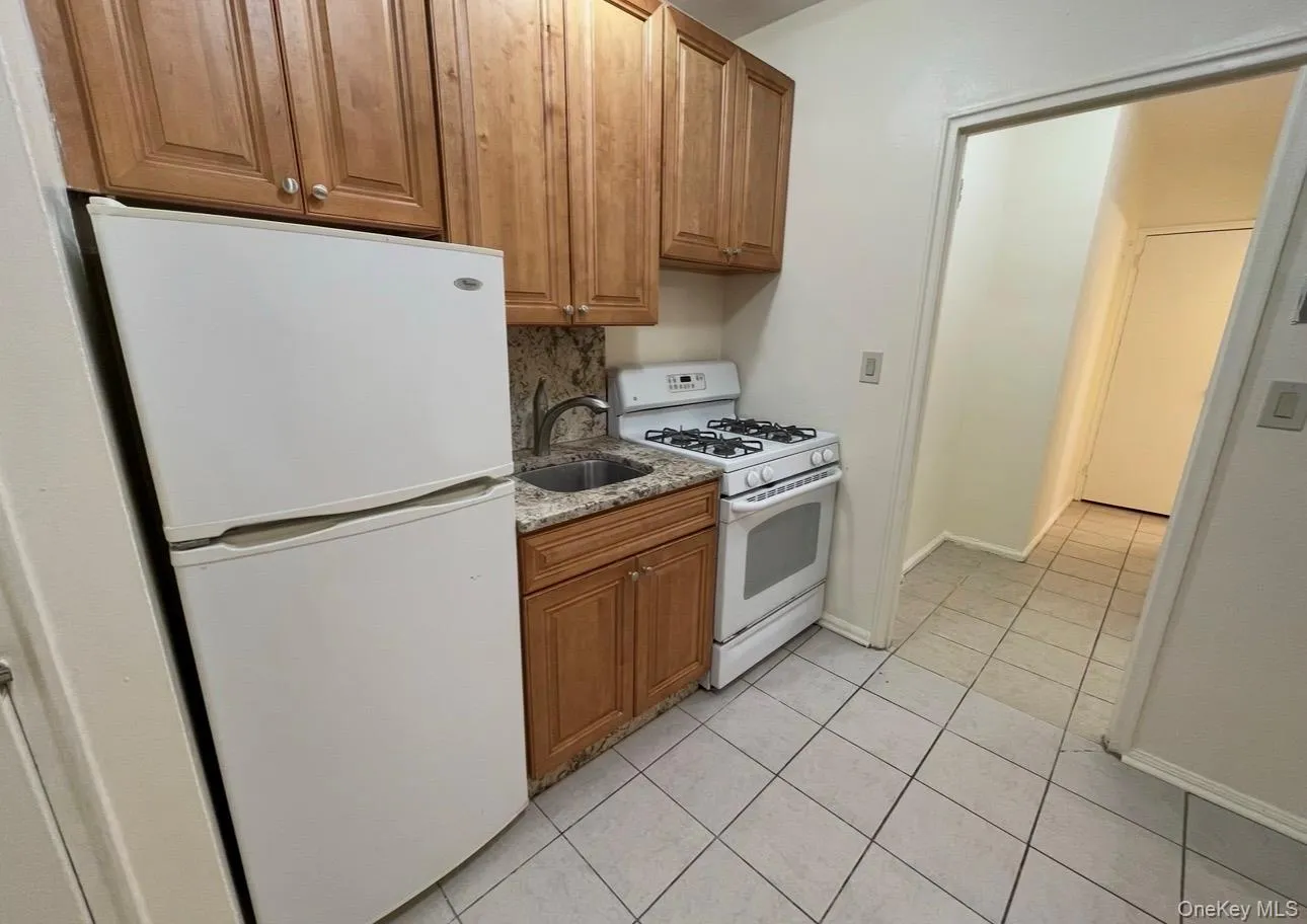 Kitchen with white appliances, brown cabinetry, light tile patterned flooring, light stone counters, and decorative backsplash Kitchen with white appliances, brown cabinetry, light tile patterned flooring, light stone counters, and decorative backsplash