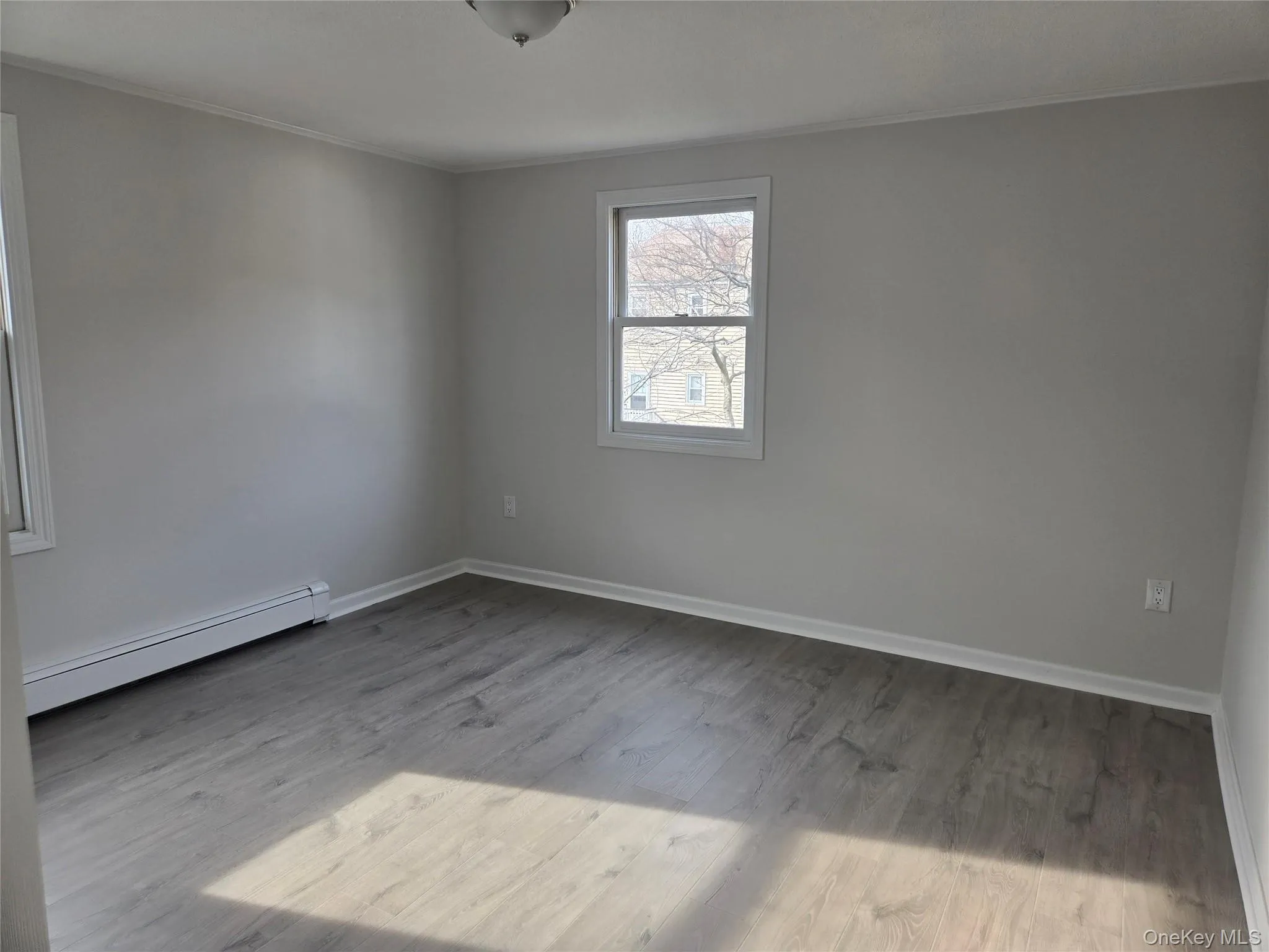 Empty room with a baseboard radiator, ornamental molding, and light wood-style floors Empty room with a baseboard radiator, ornamental molding, and light wood-style floors