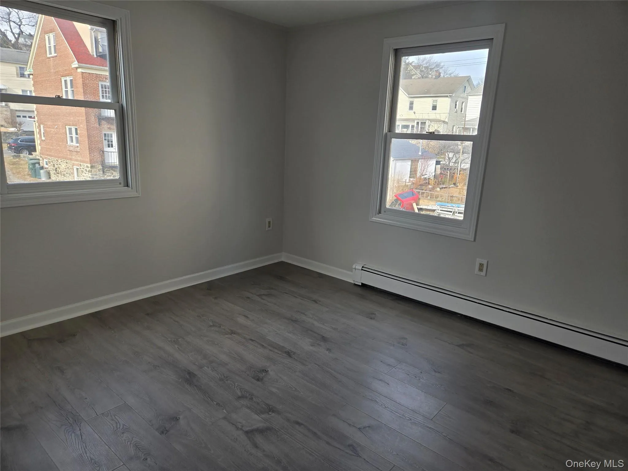 Spare room featuring a baseboard radiator, dark wood-type flooring, and healthy amount of natural light Spare room featuring a baseboard radiator, dark wood-type flooring, and healthy amount of natural light