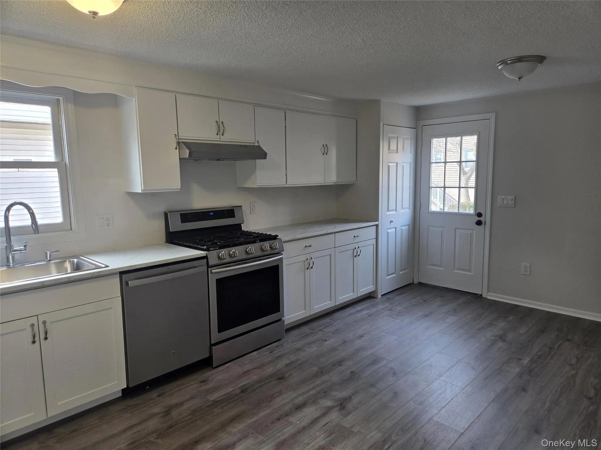 Kitchen with white cabinets, stainless steel appliances, light countertops, a textured ceiling, and dark wood-style floors Kitchen with white cabinets, stainless steel appliances, light countertops, a textured ceiling, and dark wood-style floors