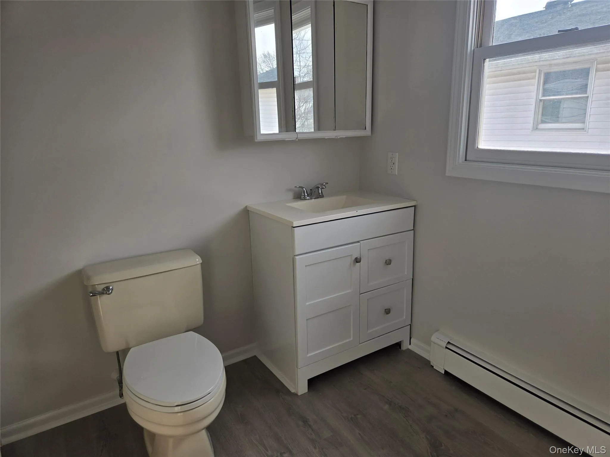 Half bathroom featuring baseboard heating, vanity, dark wood-style floors, and plenty of natural light Half bathroom featuring baseboard heating, vanity, dark wood-style floors, and plenty of natural light