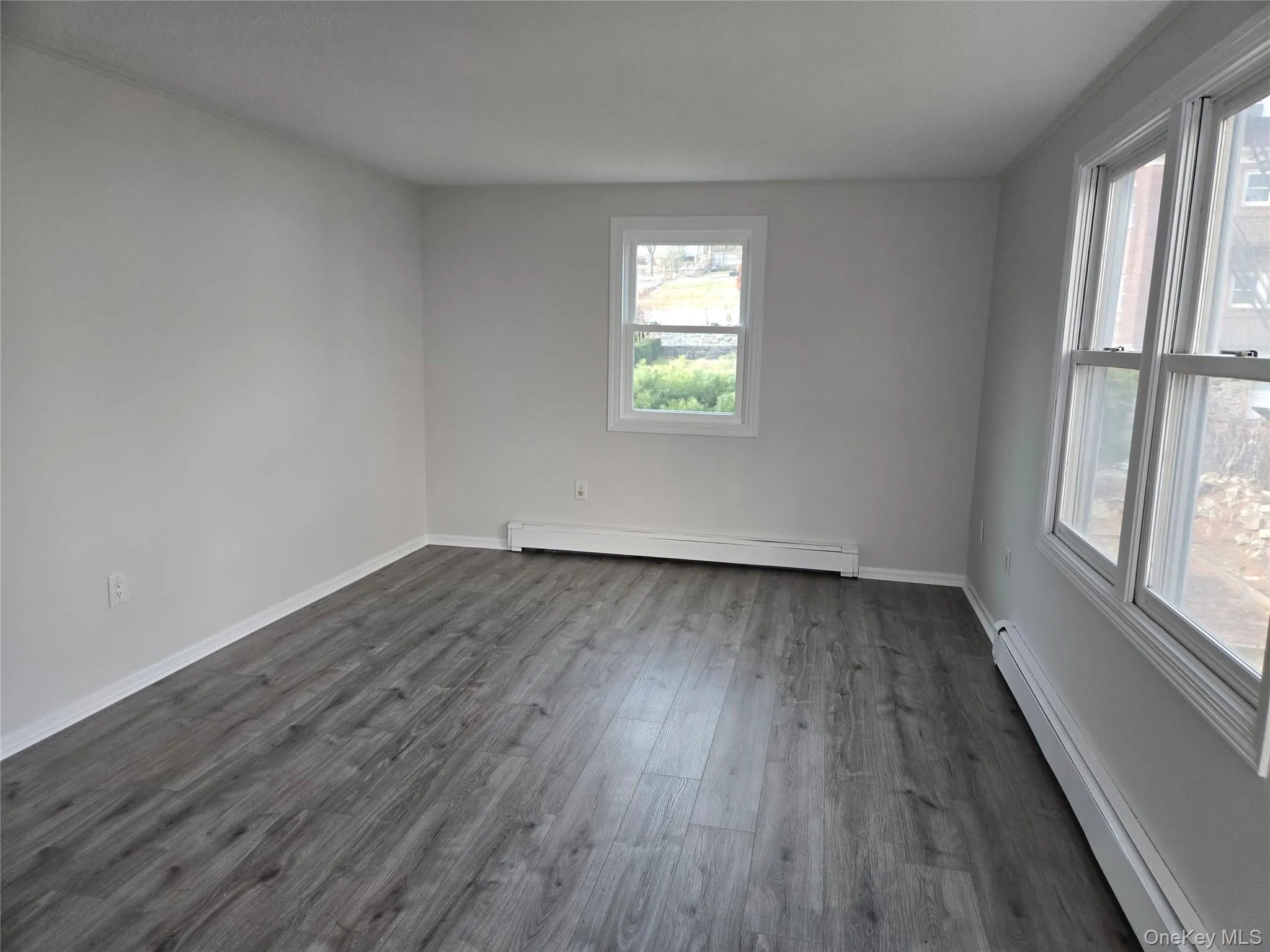 Unfurnished room with baseboard heating and dark wood finished floors Unfurnished room with baseboard heating and dark wood finished floors