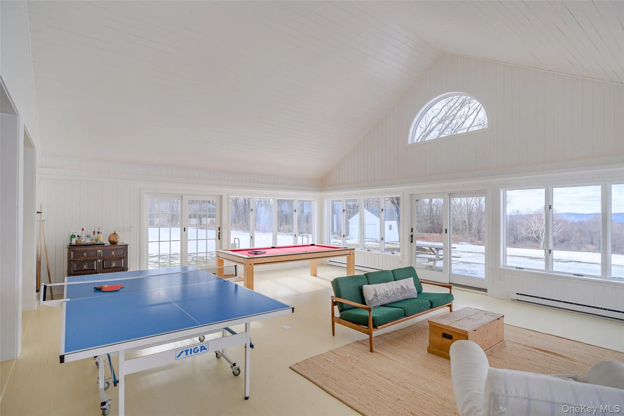 Recreation room with plenty of natural light, high vaulted ceiling, a baseboard radiator, wood walls, and billiards table Recreation room with plenty of natural light, high vaulted ceiling, a baseboard radiator, wood walls, and billiards table