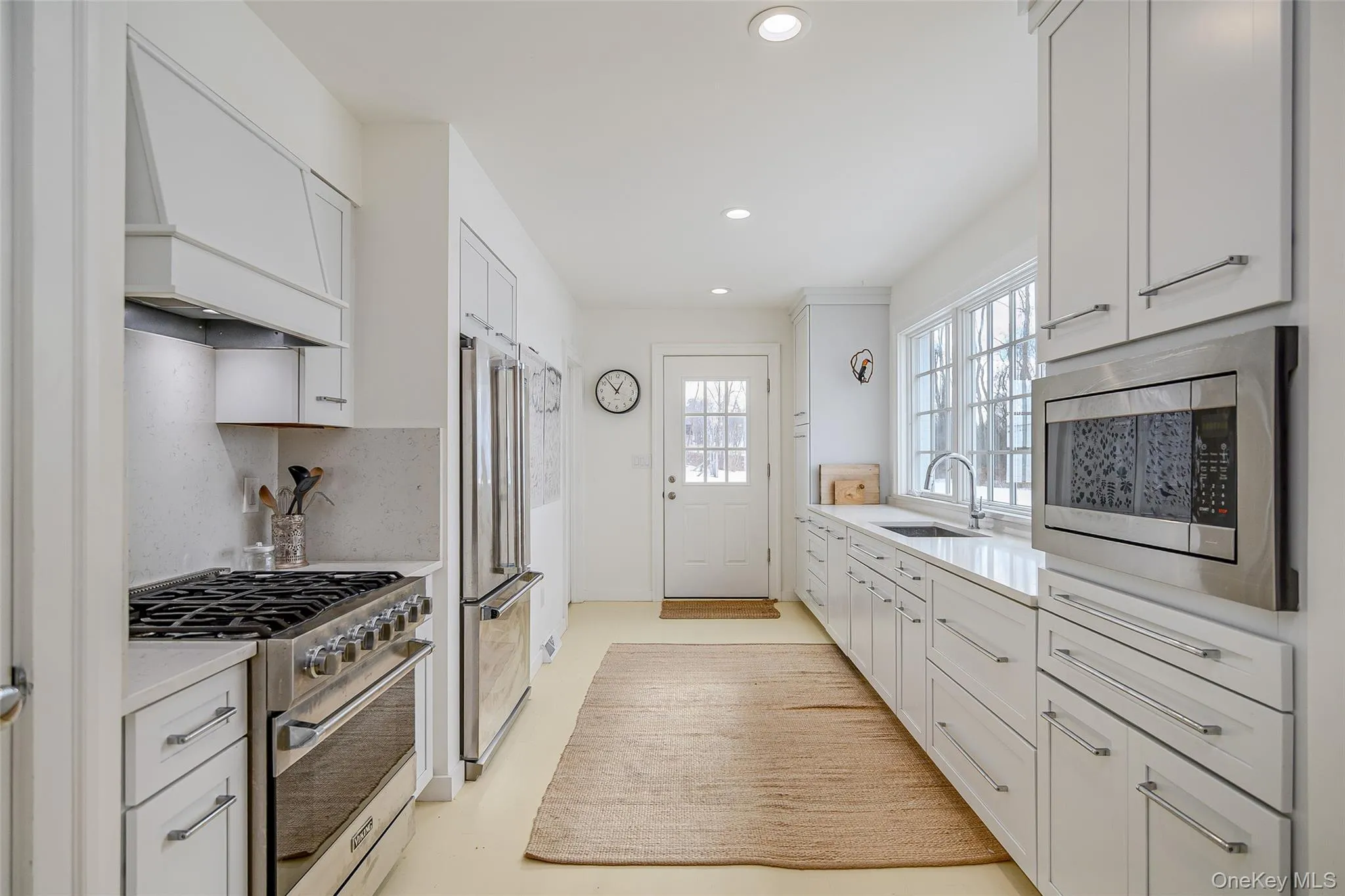 Kitchen with high quality appliances, white cabinetry, premium range hood, recessed lighting, and backsplash Kitchen with high quality appliances, white cabinetry, premium range hood, recessed lighting, and backsplash