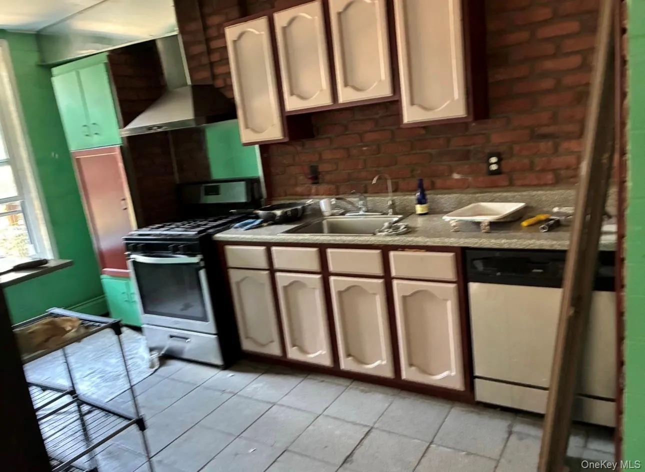 Kitchen featuring stainless steel range with gas stovetop, wall chimney range hood, light countertops, dishwasher, and brick wall Kitchen featuring stainless steel range with gas stovetop, wall chimney range hood, light countertops, dishwasher, and brick wall
