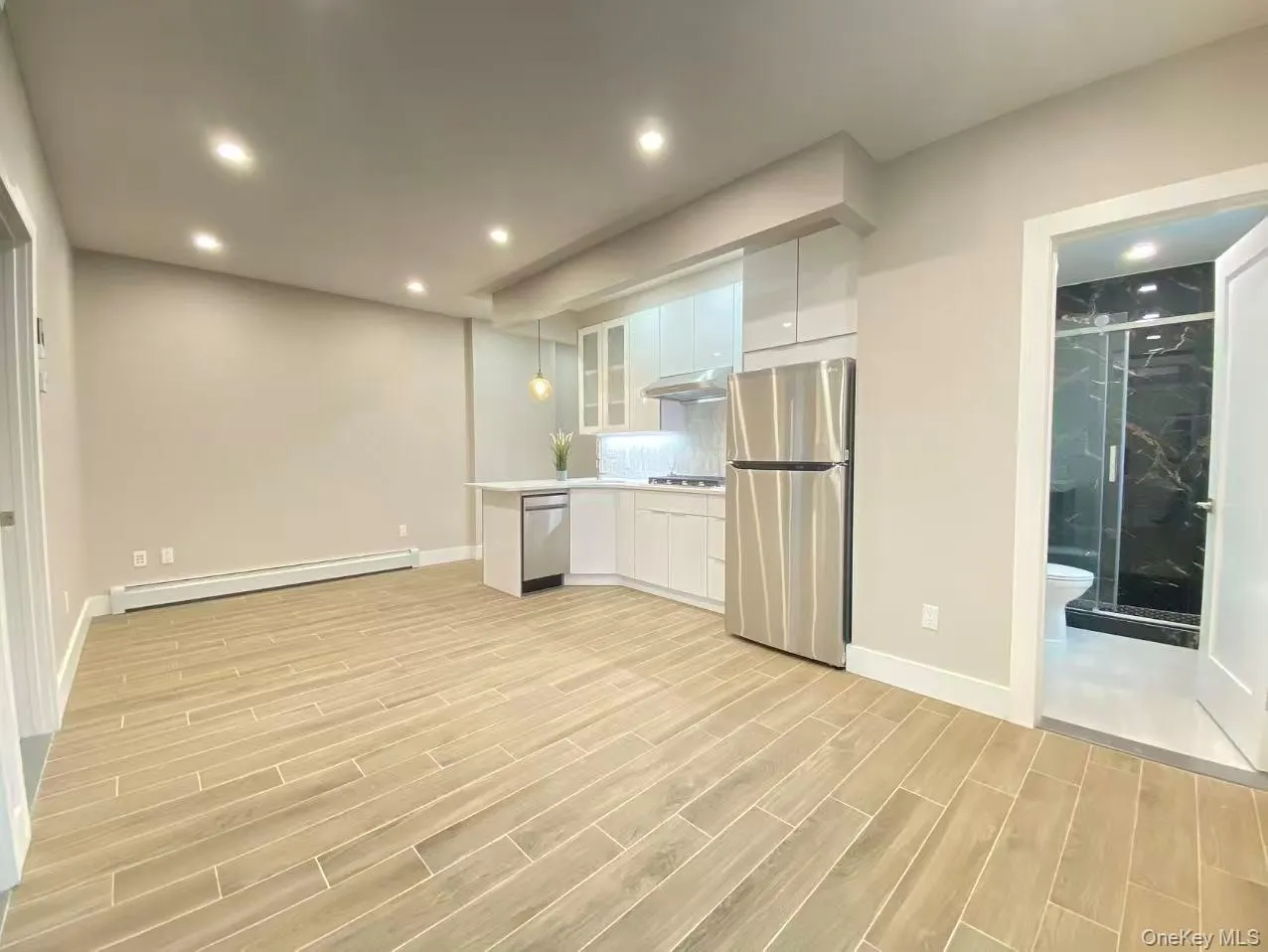 Kitchen with white cabinets, light countertops, stainless steel appliances, glass insert cabinets, and baseboard heating Kitchen with white cabinets, light countertops, stainless steel appliances, glass insert cabinets, and baseboard heating