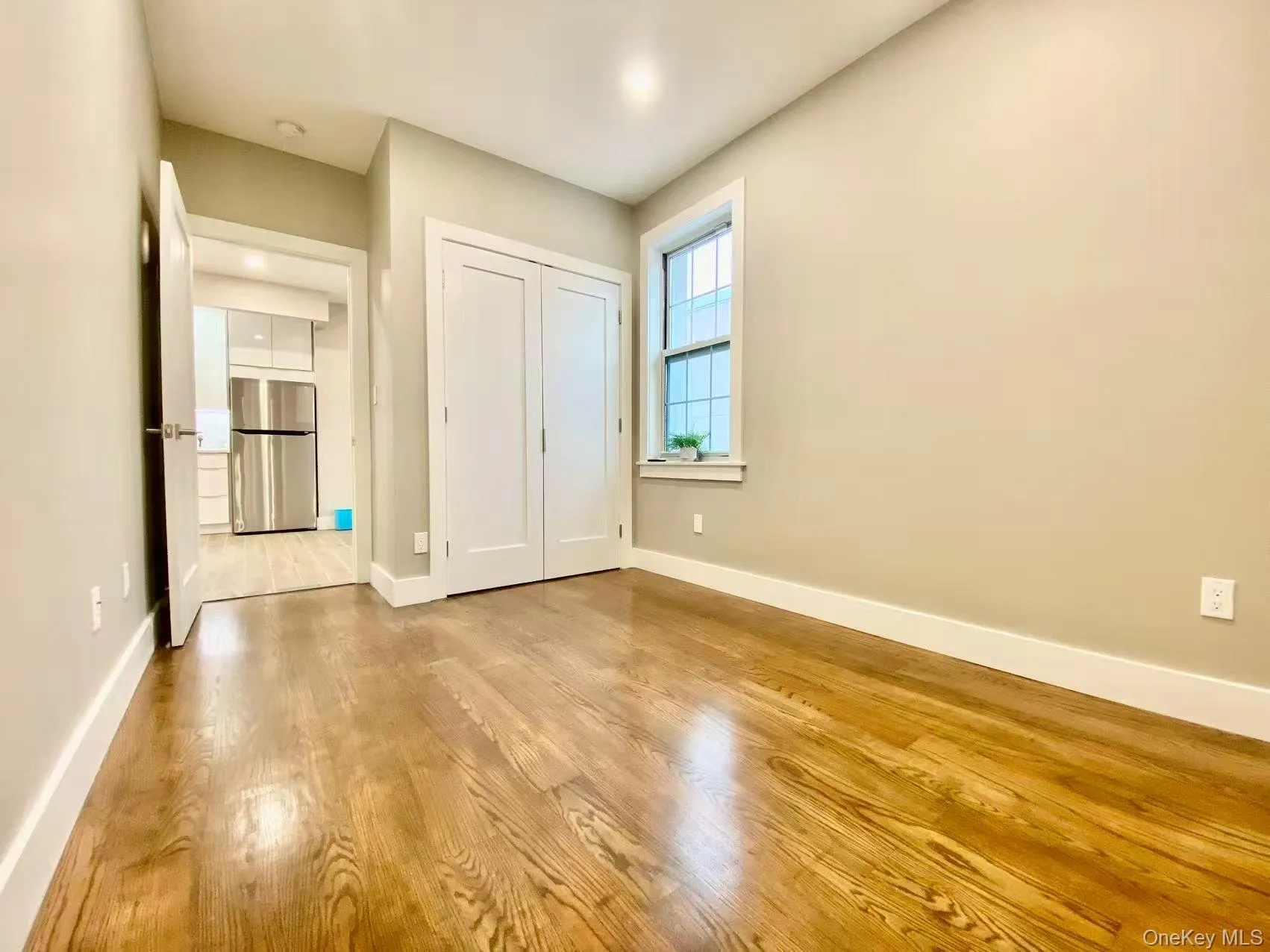 Unfurnished bedroom featuring freestanding refrigerator, wood finished floors, and a closet Unfurnished bedroom featuring freestanding refrigerator, wood finished floors, and a closet