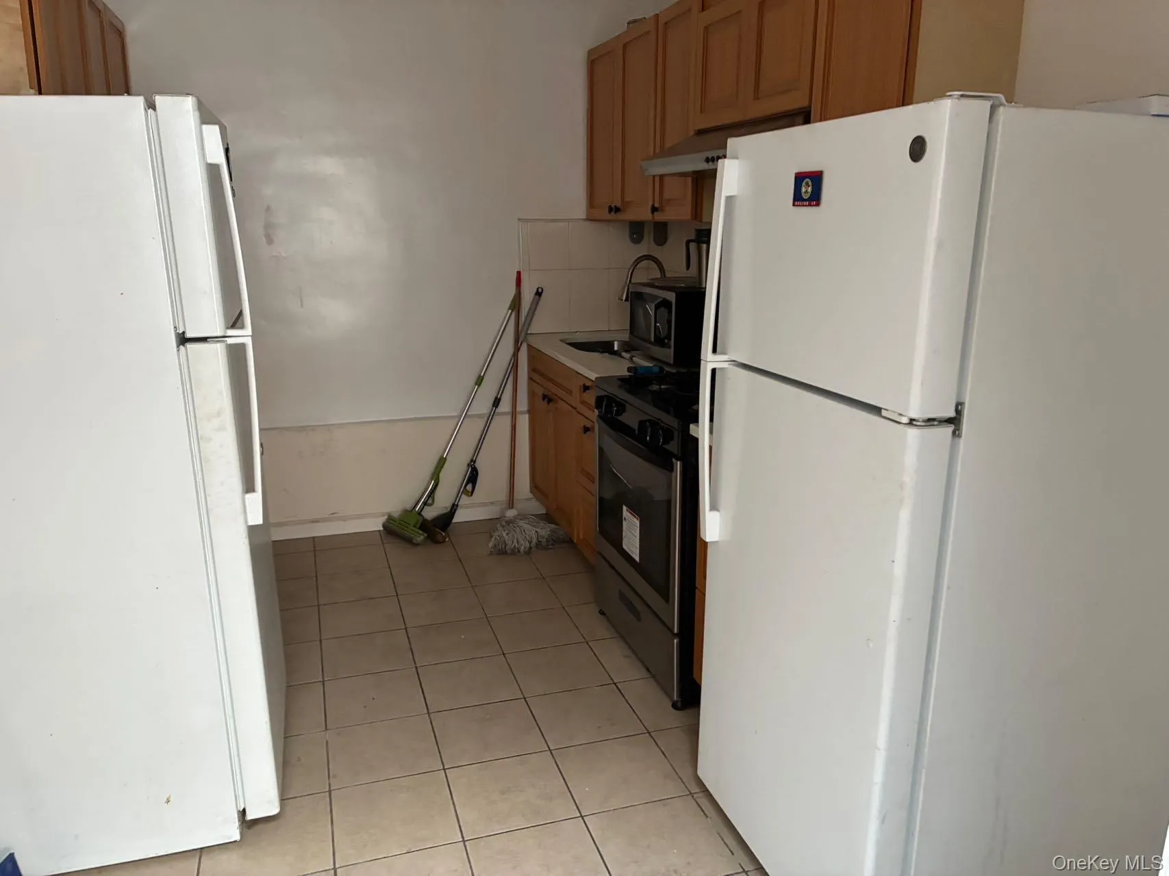 Kitchen with stainless steel appliances, light countertops, light tile patterned floors, under cabinet range hood, and backsplash Kitchen with stainless steel appliances, light countertops, light tile patterned floors, under cabinet range hood, and backsplash