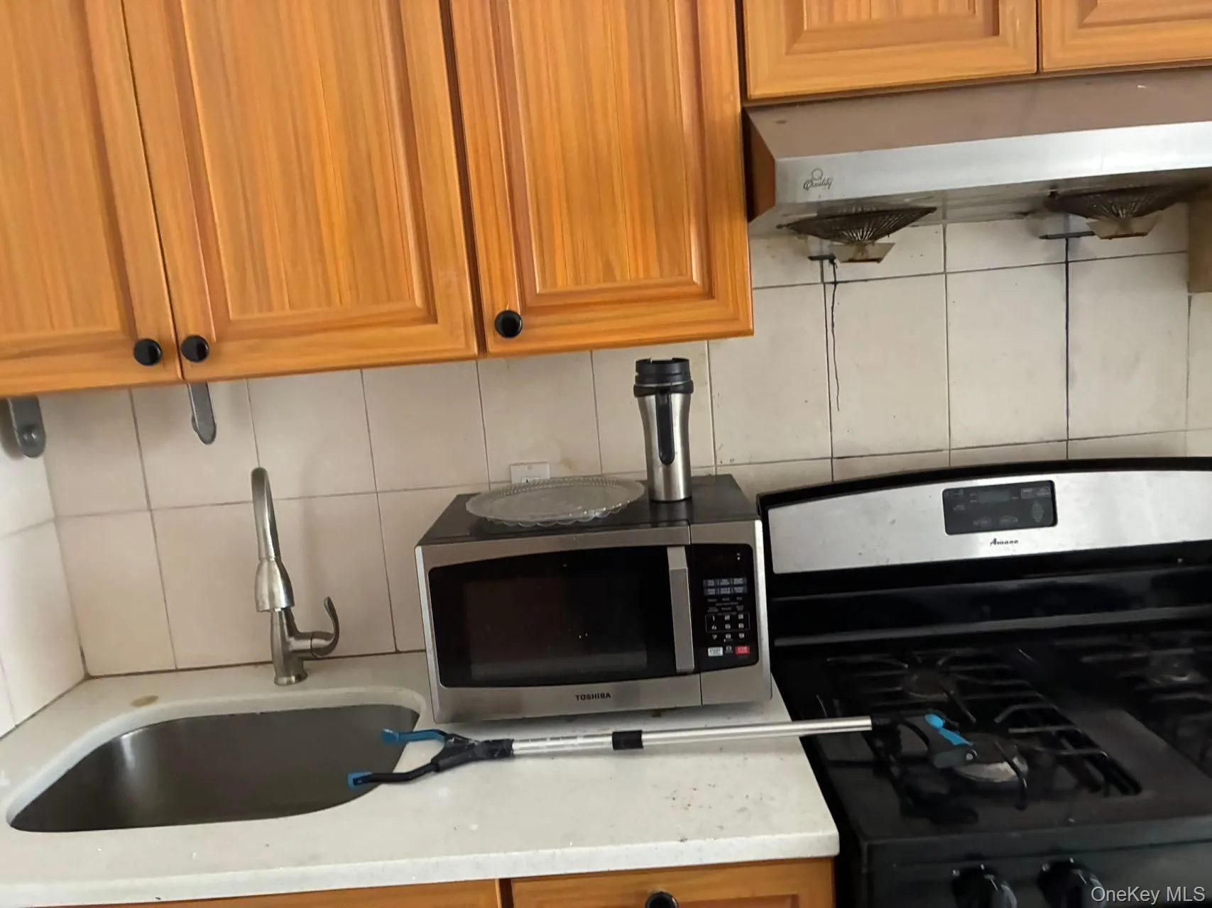 Kitchen view of appliances with stainless steel finishes, backsplash, brown cabinets, under cabinet range hood, and light stone counters Kitchen view of appliances with stainless steel finishes, backsplash, brown cabinets, under cabinet range hood, and light stone counters