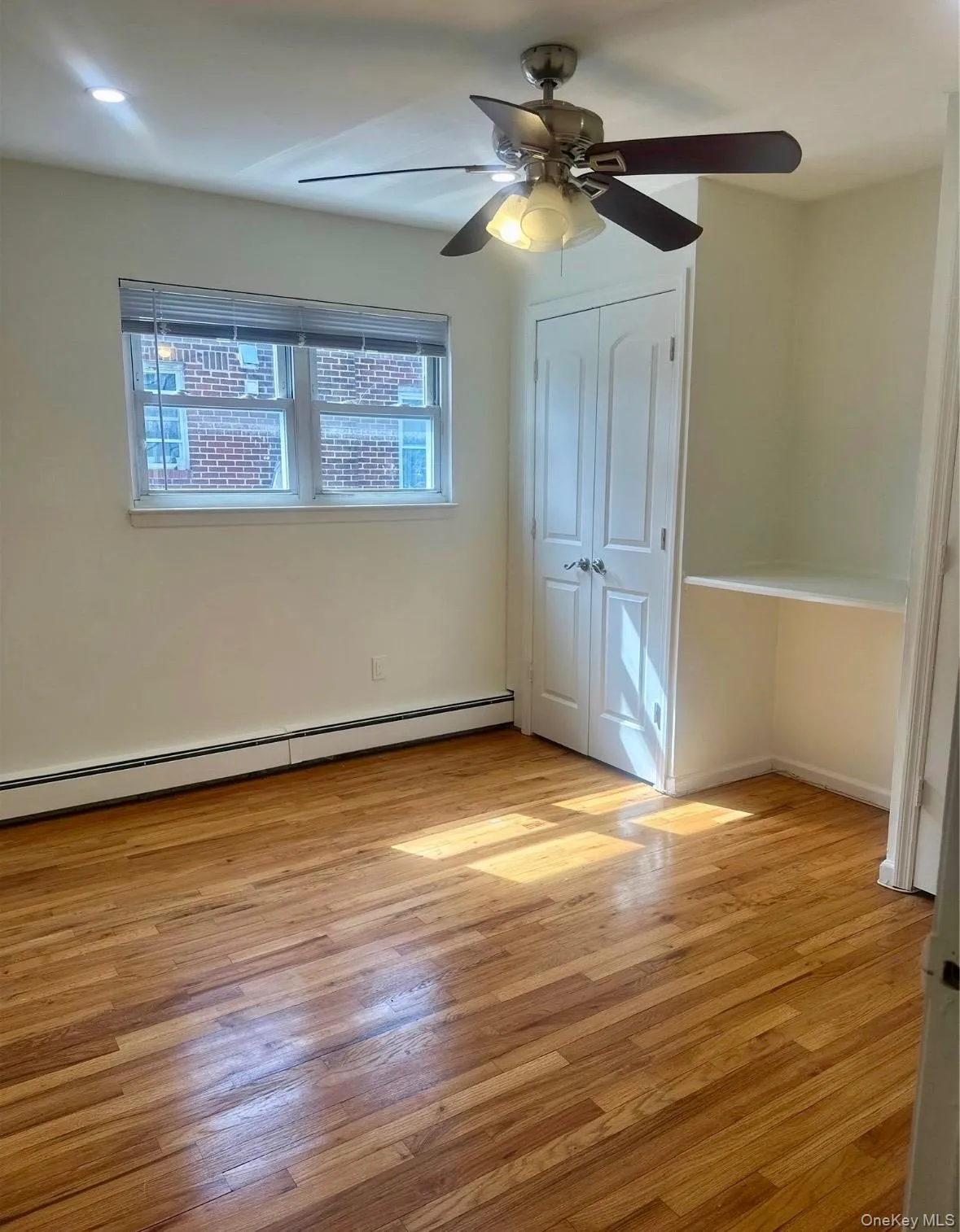 Unfurnished bedroom with baseboard heating, light wood-type flooring, a ceiling fan, and a closet Unfurnished bedroom with baseboard heating, light wood-type flooring, a ceiling fan, and a closet