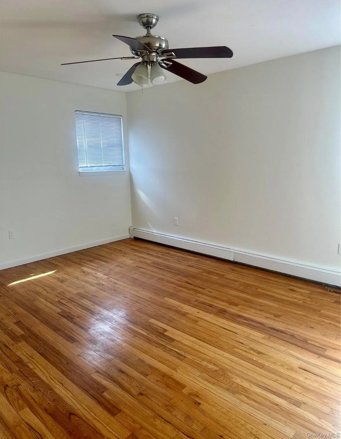 Spare room with a baseboard radiator, light wood finished floors, and a ceiling fan Spare room with a baseboard radiator, light wood finished floors, and a ceiling fan
