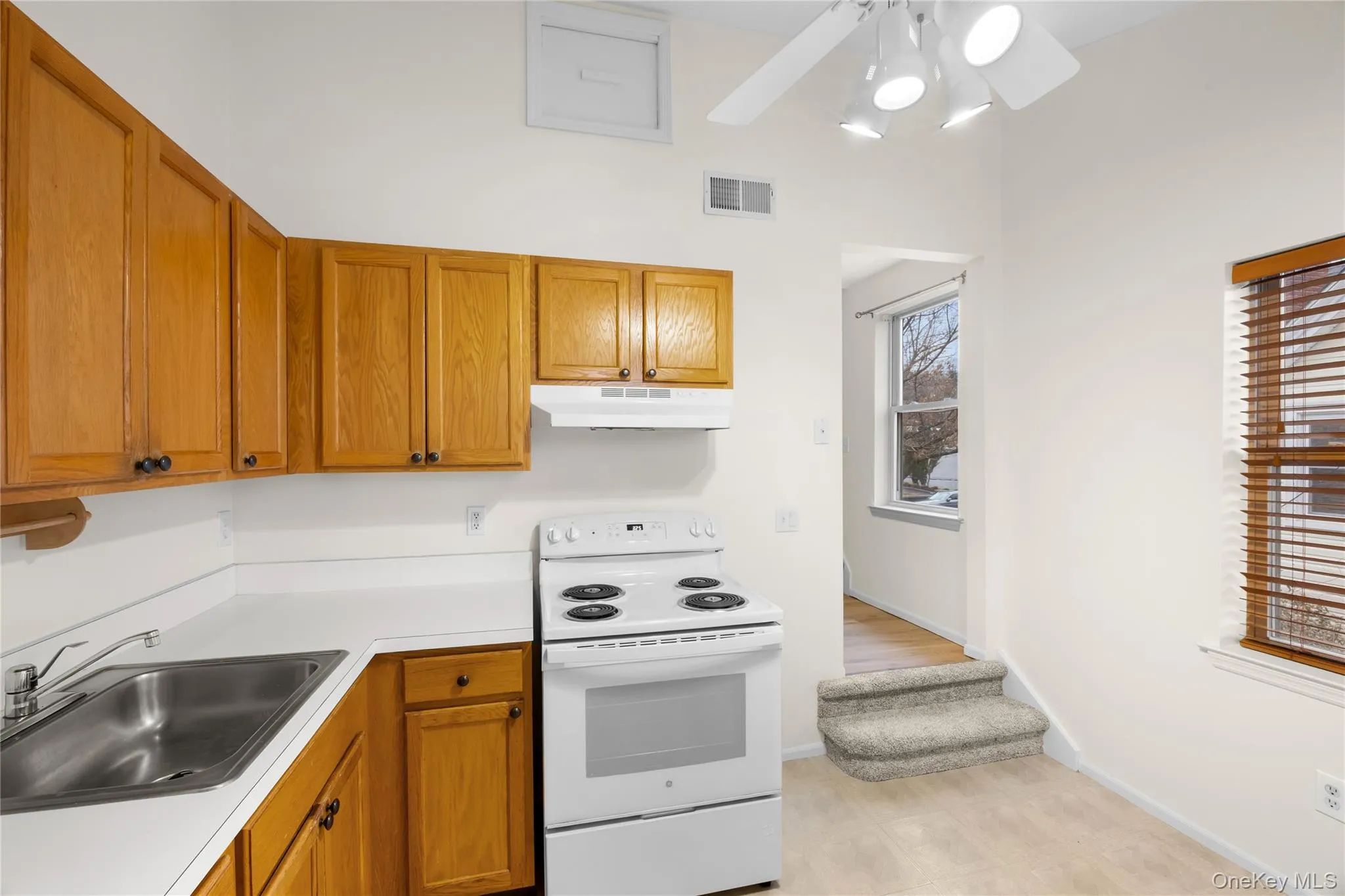Kitchen with brown cabinetry, white range with electric cooktop, light countertops, under cabinet range hood, and ceiling fan Kitchen with brown cabinetry, white range with electric cooktop, light countertops, under cabinet range hood, and ceiling fan