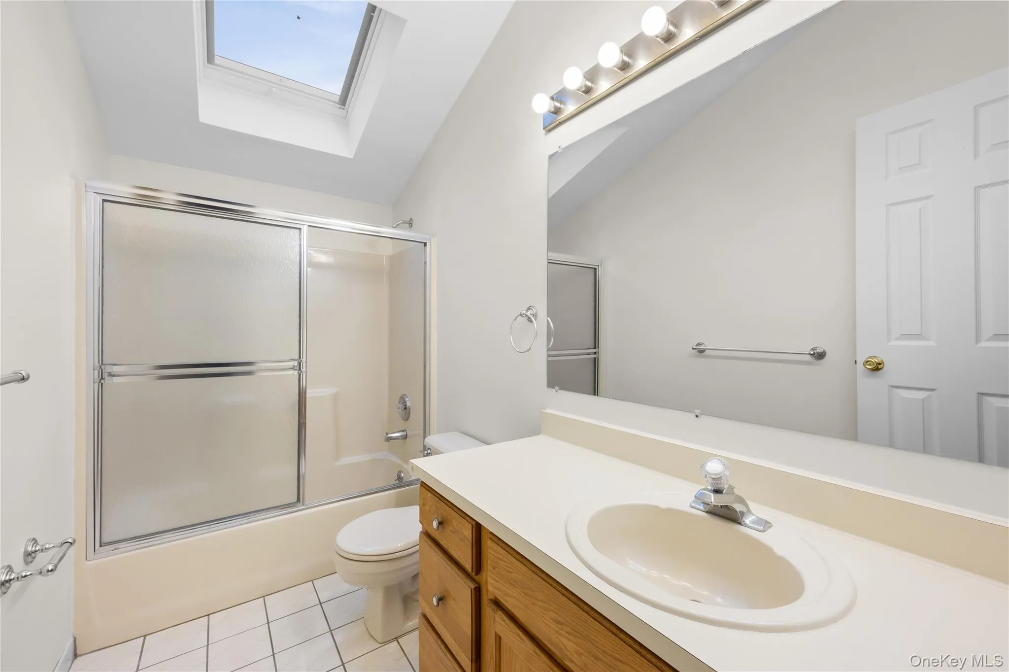 Full bath with a skylight, vanity, bath / shower combo with glass door, light tile patterned floors, and lofted ceiling Full bath with a skylight, vanity, bath / shower combo with glass door, light tile patterned floors, and lofted ceiling