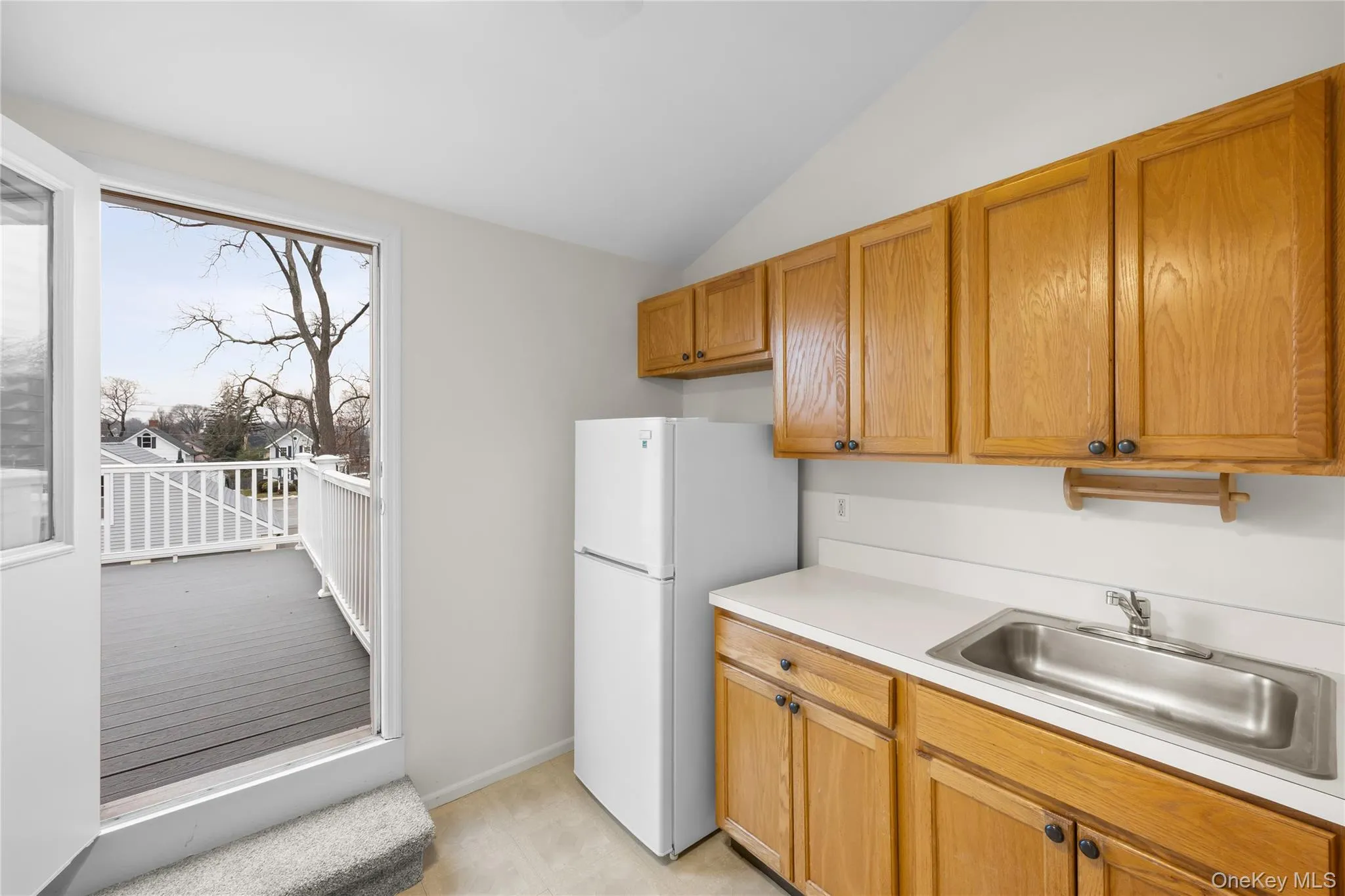Kitchen featuring light countertops, freestanding refrigerator, brown cabinets, and vaulted ceiling Kitchen featuring light countertops, freestanding refrigerator, brown cabinets, and vaulted ceiling