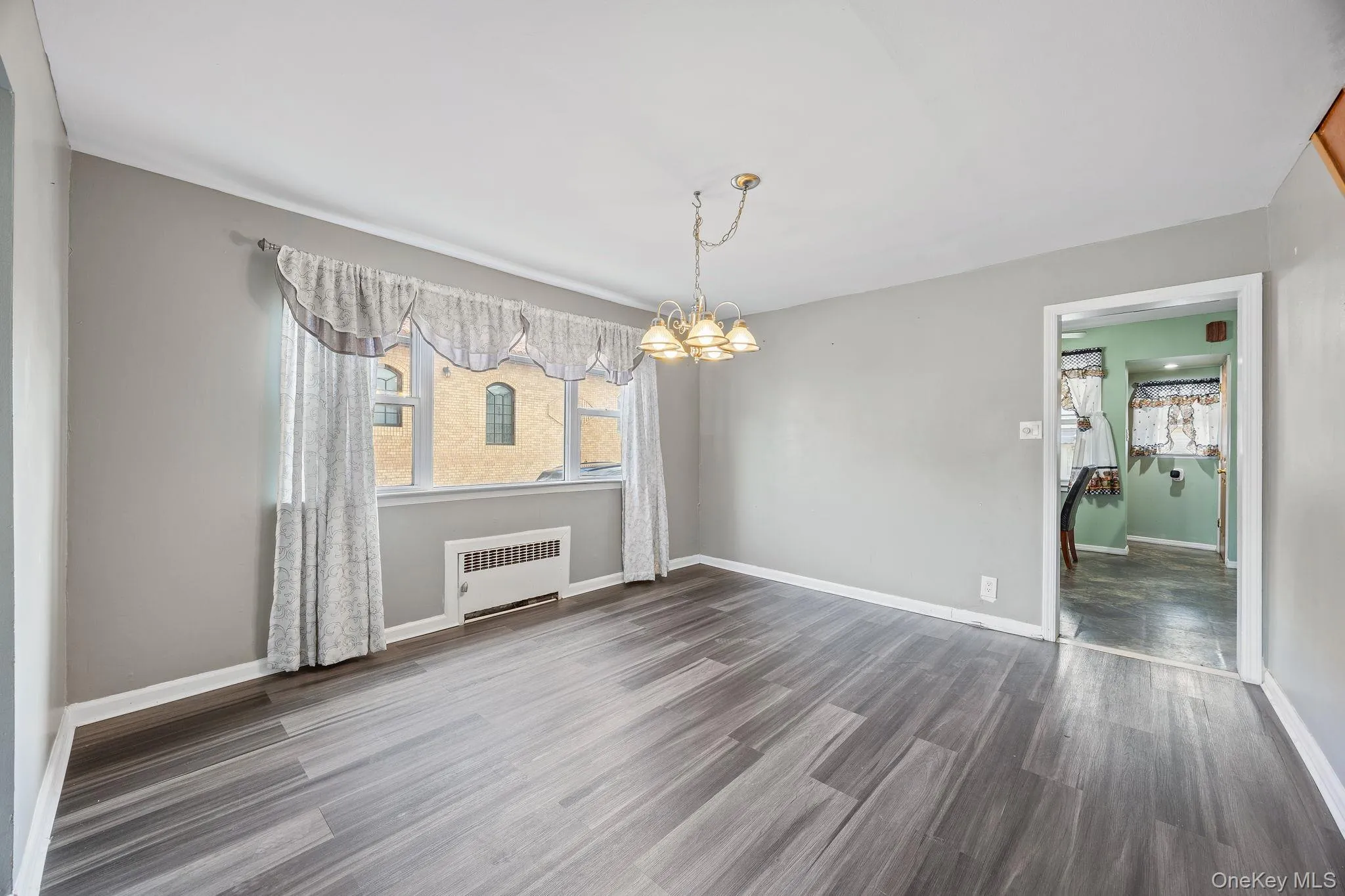 Unfurnished dining area with a chandelier, radiator heating unit, and dark wood-style flooring Unfurnished dining area with a chandelier, radiator heating unit, and dark wood-style flooring
