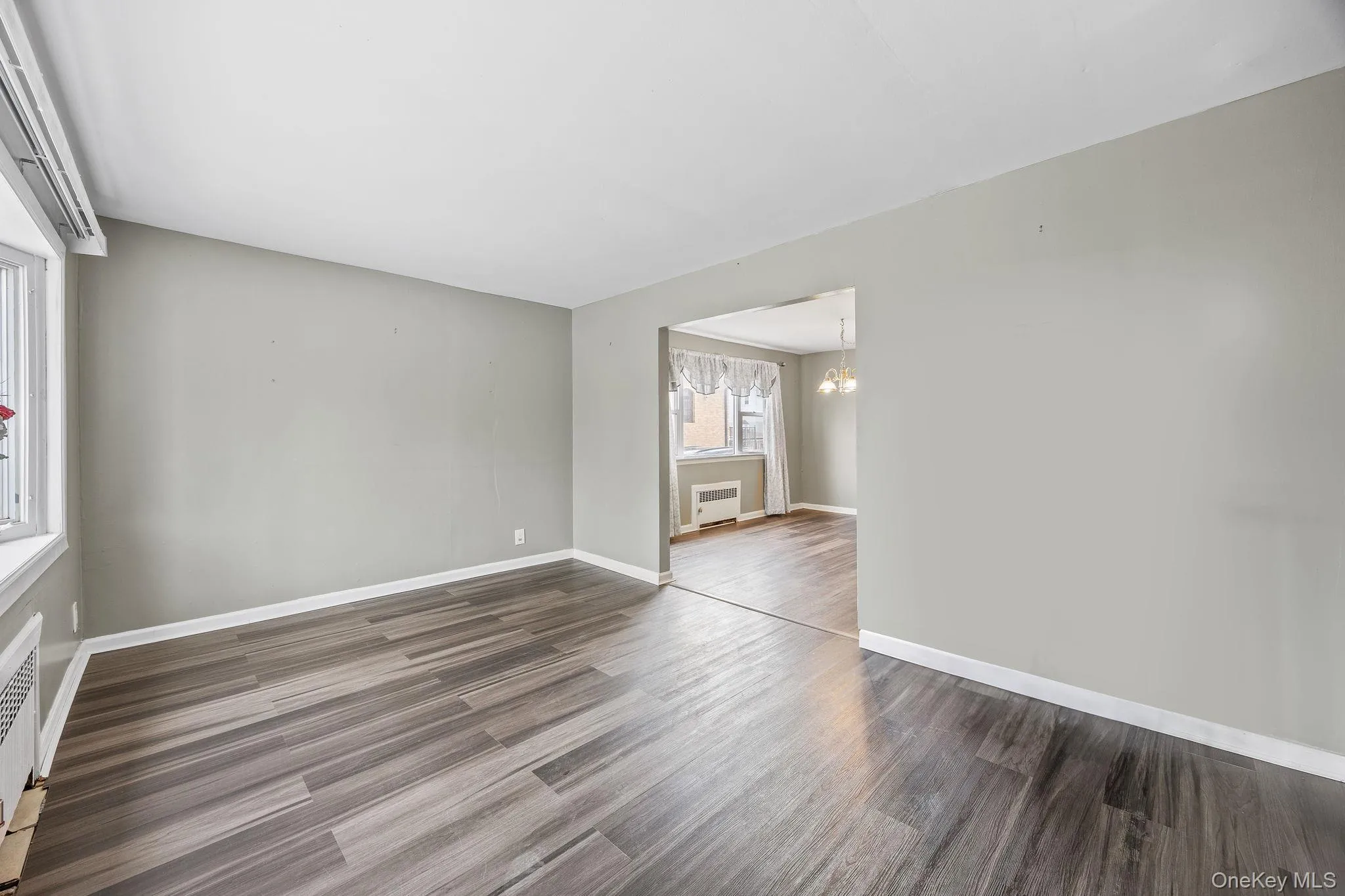 Empty room with dark wood finished floors, a chandelier, and radiator heating unit Empty room with dark wood finished floors, a chandelier, and radiator heating unit