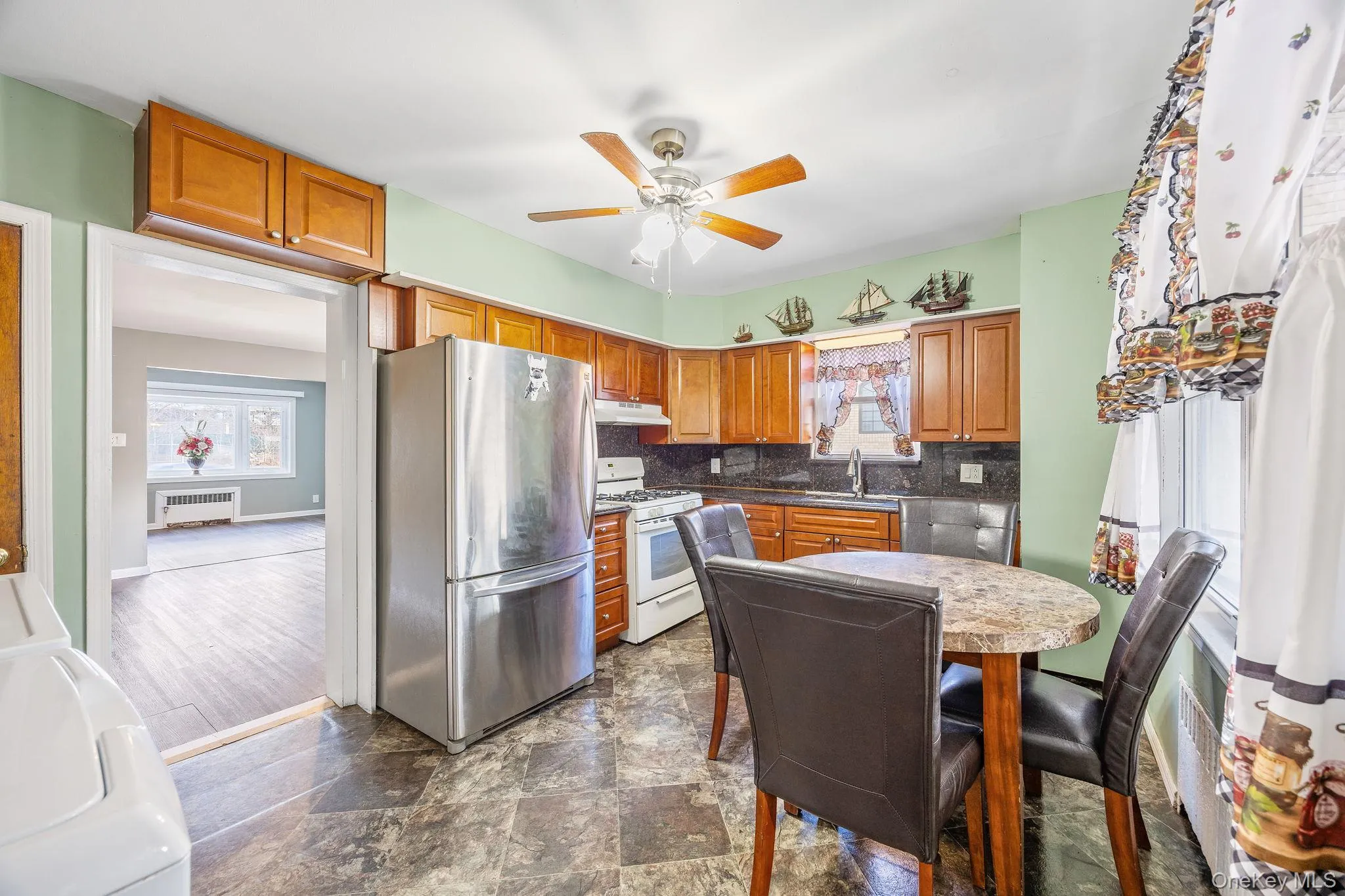 Kitchen featuring freestanding refrigerator, brown cabinets, white gas range oven, and plenty of natural light Kitchen featuring freestanding refrigerator, brown cabinets, white gas range oven, and plenty of natural light