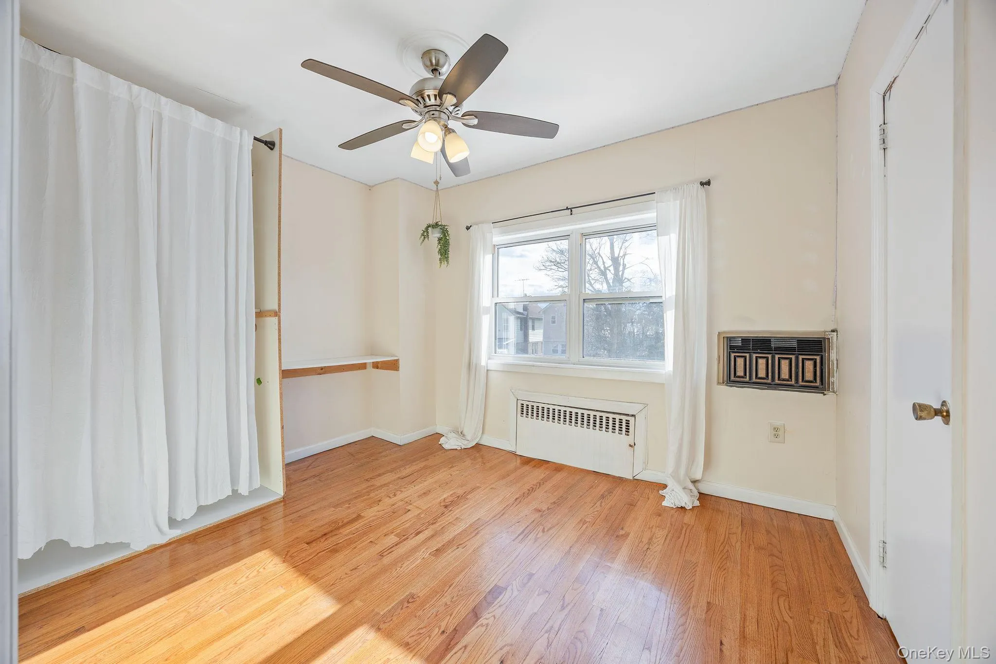 Unfurnished room with light wood-type flooring, radiator heating unit, and a ceiling fan Unfurnished room with light wood-type flooring, radiator heating unit, and a ceiling fan