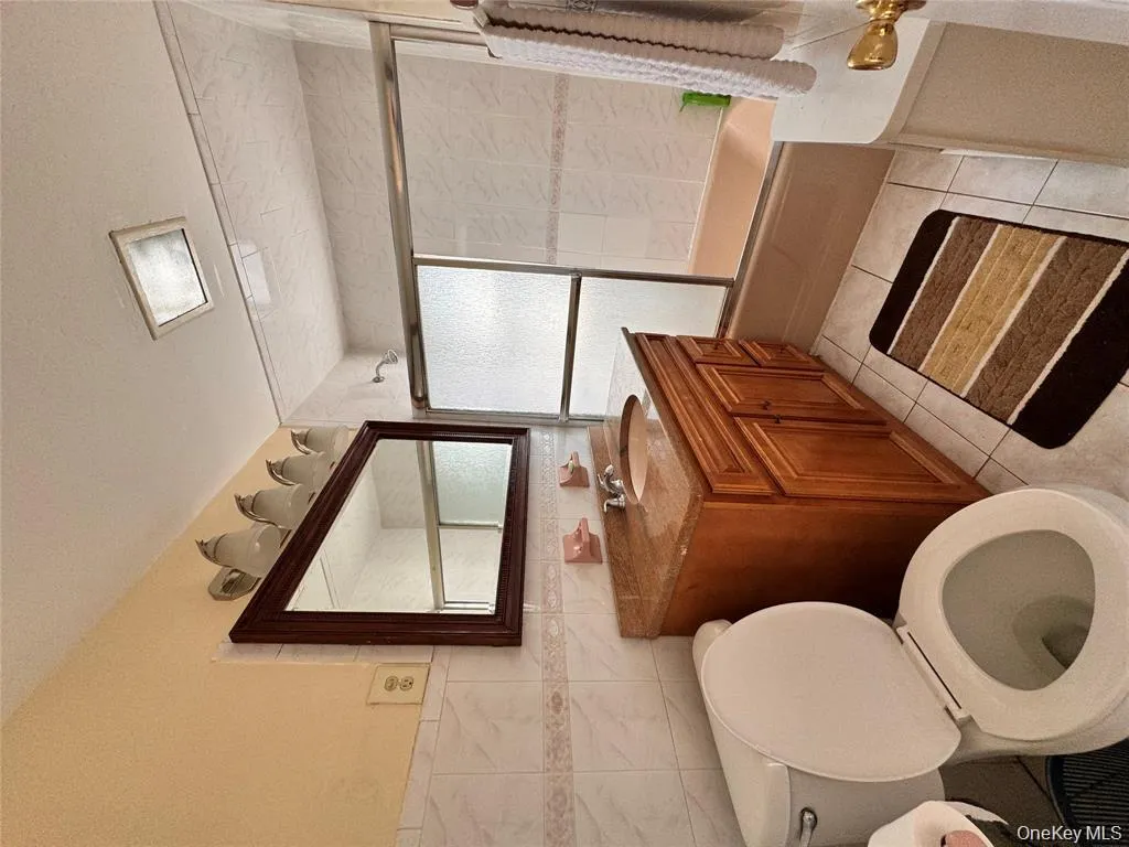 Full bath with vanity, shower / bath combination with glass door, tile walls, light tile patterned floors, and a textured ceiling Full bath with vanity, shower / bath combination with glass door, tile walls, light tile patterned floors, and a textured ceiling
