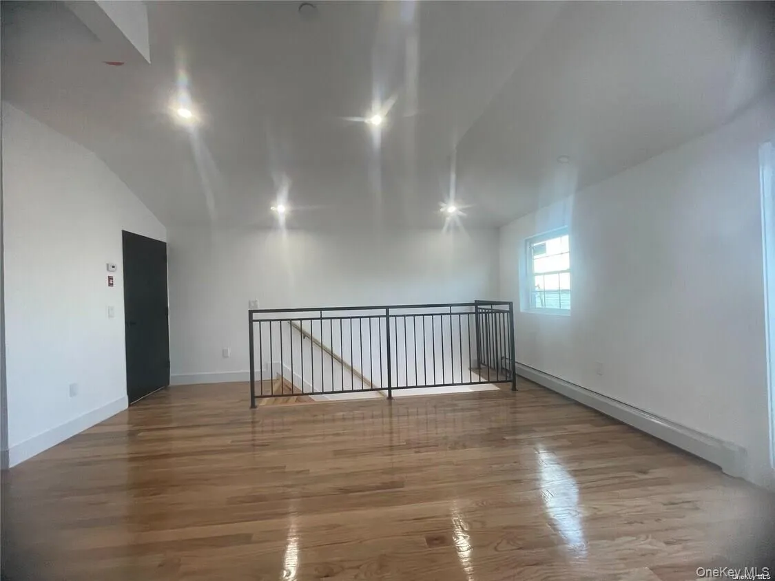 Unfurnished room featuring vaulted ceiling, light wood finished floors, and a baseboard heating unit Unfurnished room featuring vaulted ceiling, light wood finished floors, and a baseboard heating unit