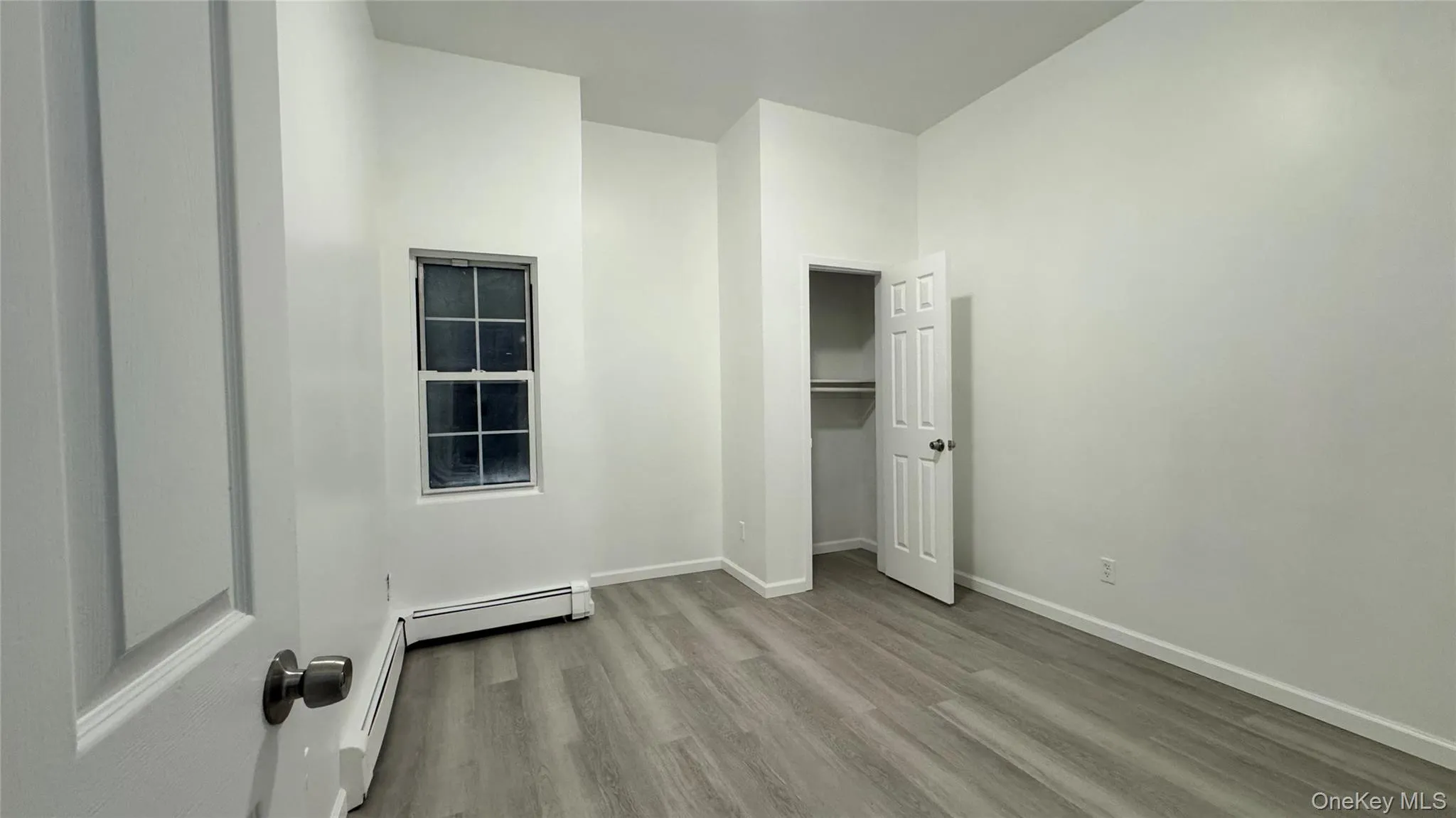 Unfurnished bedroom featuring light wood-type flooring, a closet, and a baseboard heating unit Unfurnished bedroom featuring light wood-type flooring, a closet, and a baseboard heating unit